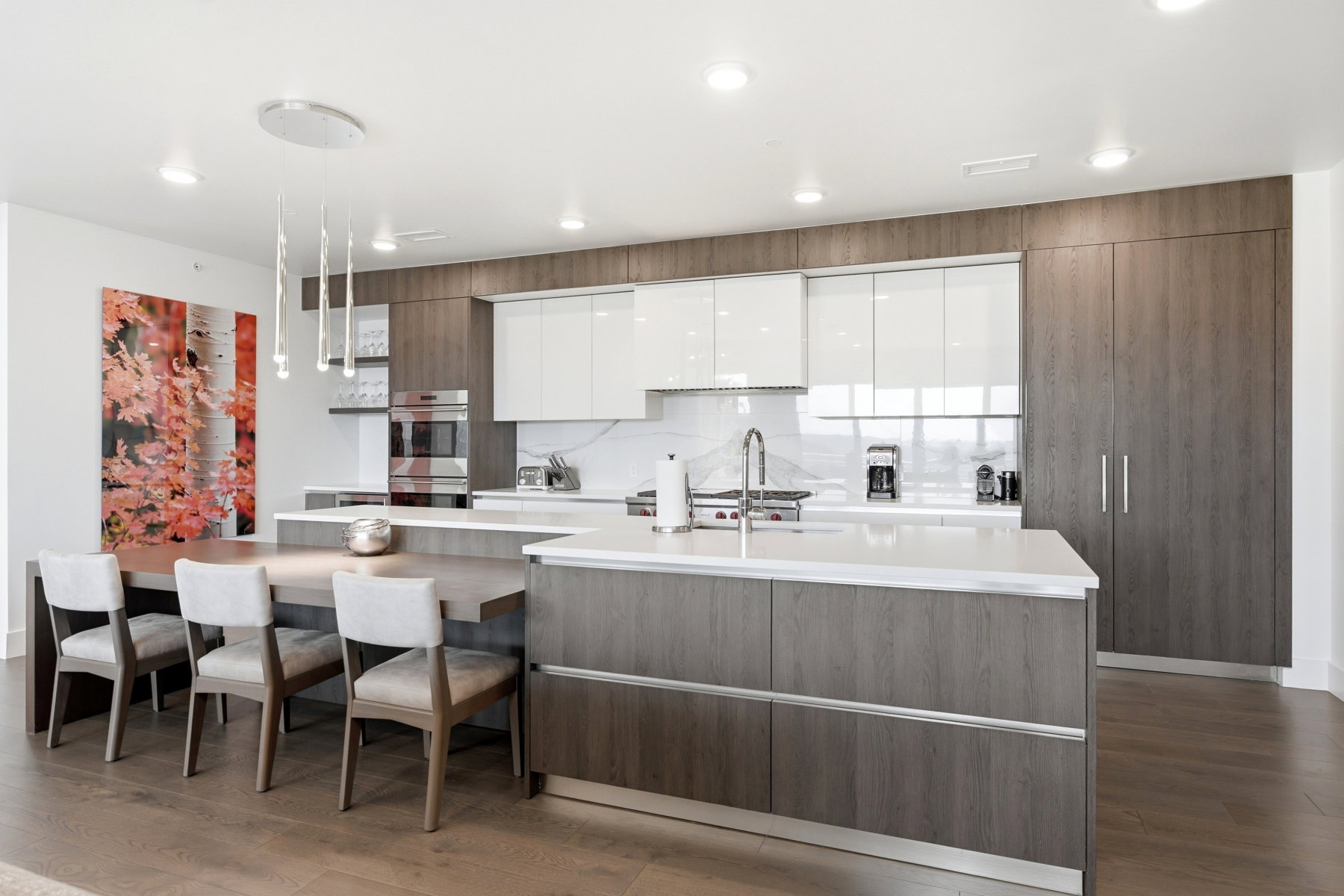 Modern kitchen featuring wood-finish flooring, a spacious island with a white countertop, and integrated appliances