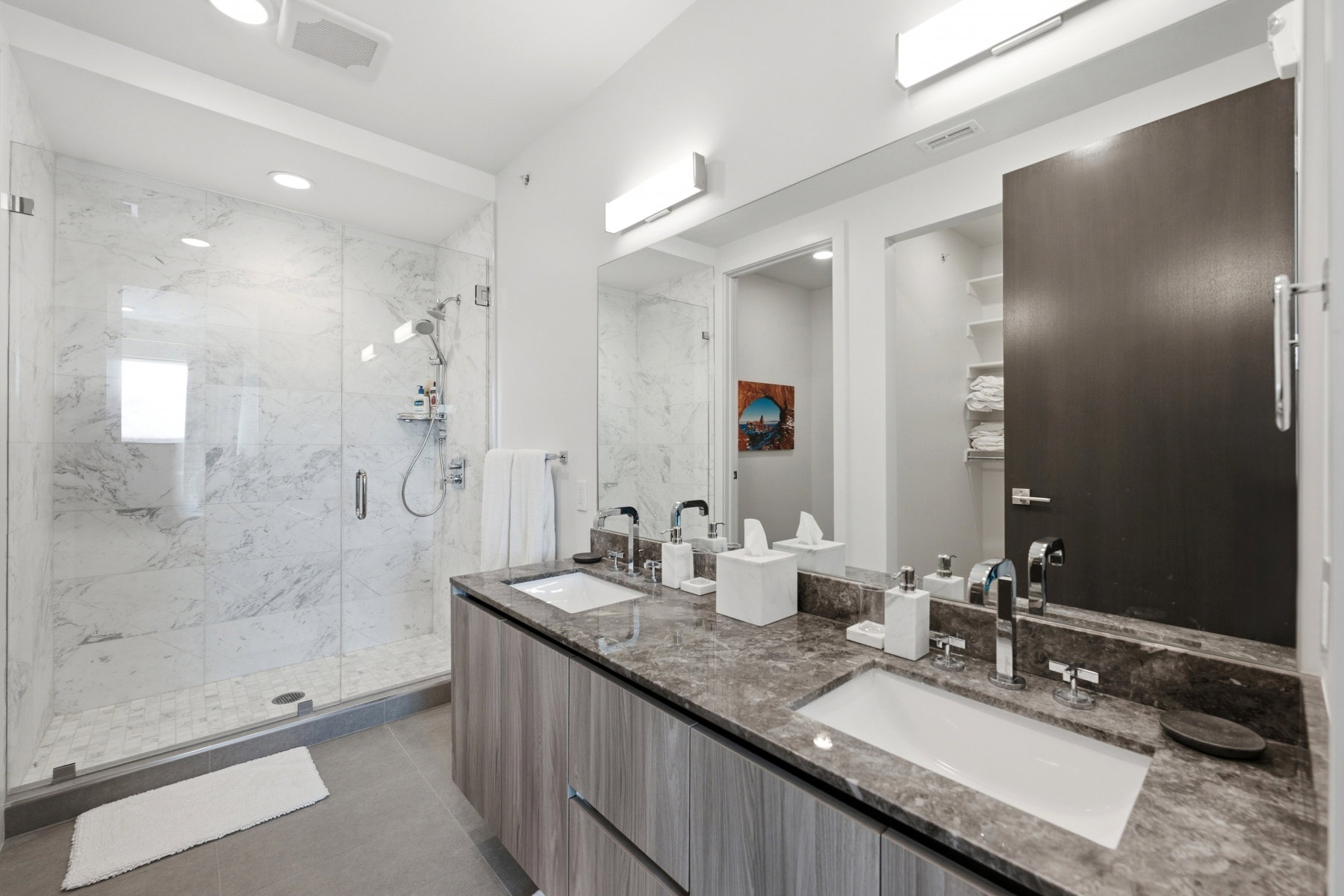 Bathroom featuring a clear glass shower enclosure with marble-patterned tile, a dual vanity with undermount sinks, and a stone-finish countertop