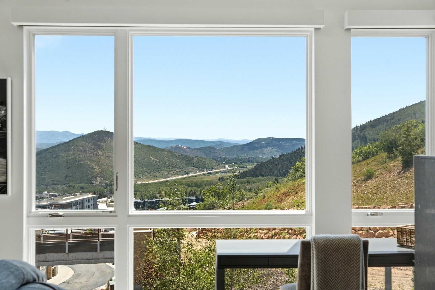 Expansive window wall showcasing a sweeping mountain panorama with distant roadways and local structures