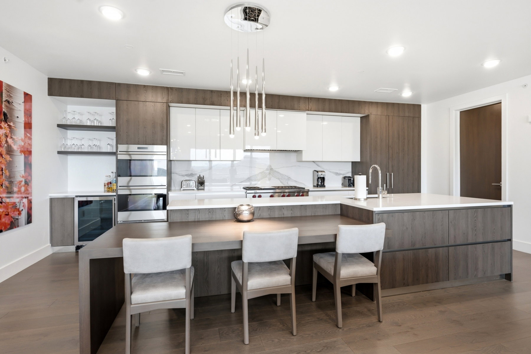 Modern kitchen featuring an extended island with seating, dark wood-finish cabinetry, bright white upper cabinets, stainless steel appliances, and a sleek pendant light fixture