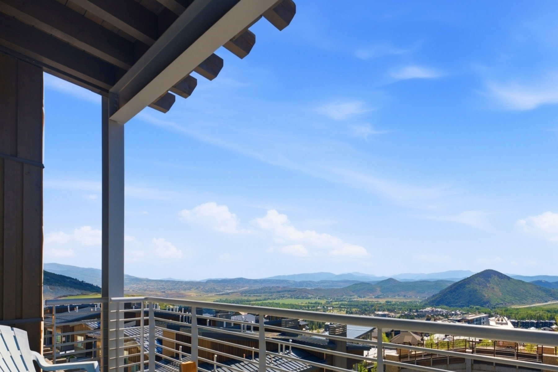 Spacious outdoor balcony with a light-colored railing, offering expansive scenery of distant mountains, clouds, and surrounding structures