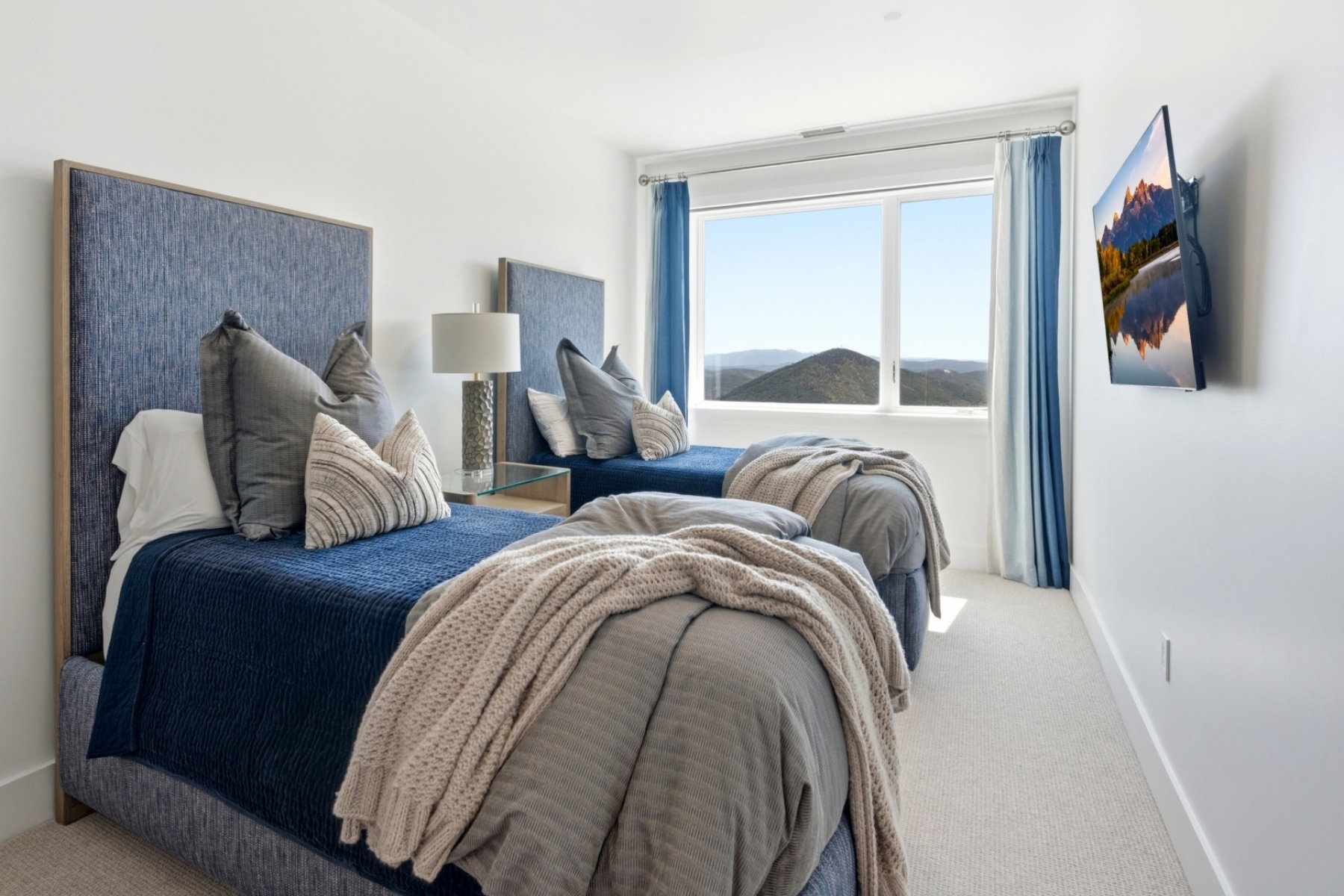 Bright interior space featuring a large window, mountain scenery, light-toned carpet flooring, and white walls