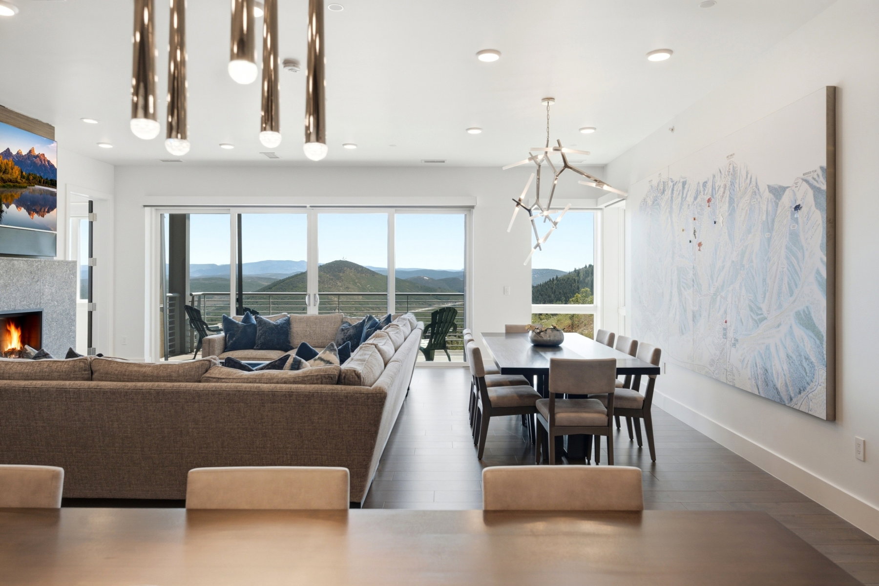 Open-concept living and dining area featuring expansive glass sliding doors, dark wood-finish flooring, a stone-clad fireplace, and a contemporary dining chandelier