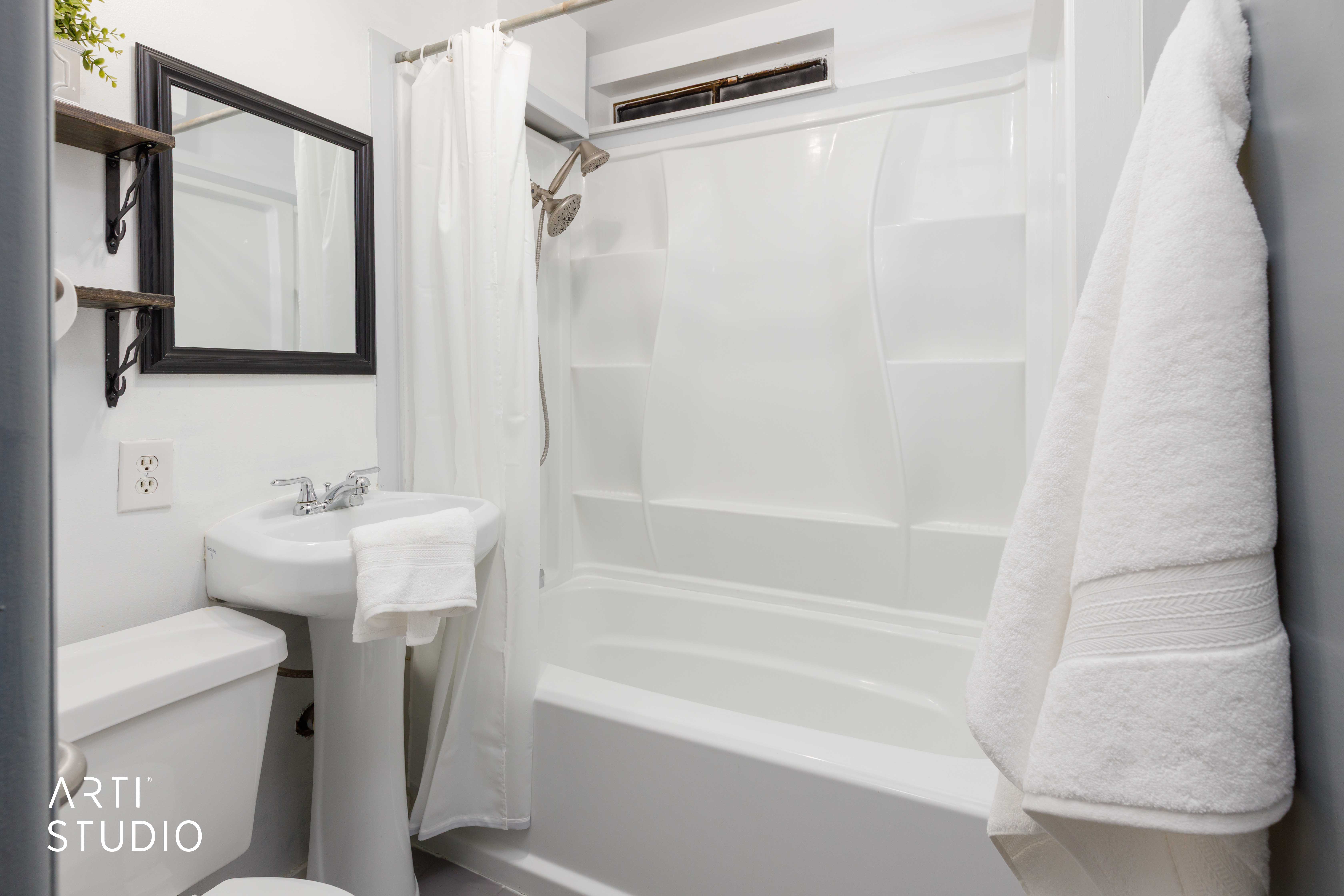 White pedestal sink with chrome faucet, a wall-mounted mirror with a black frame, and a white one-piece toilet