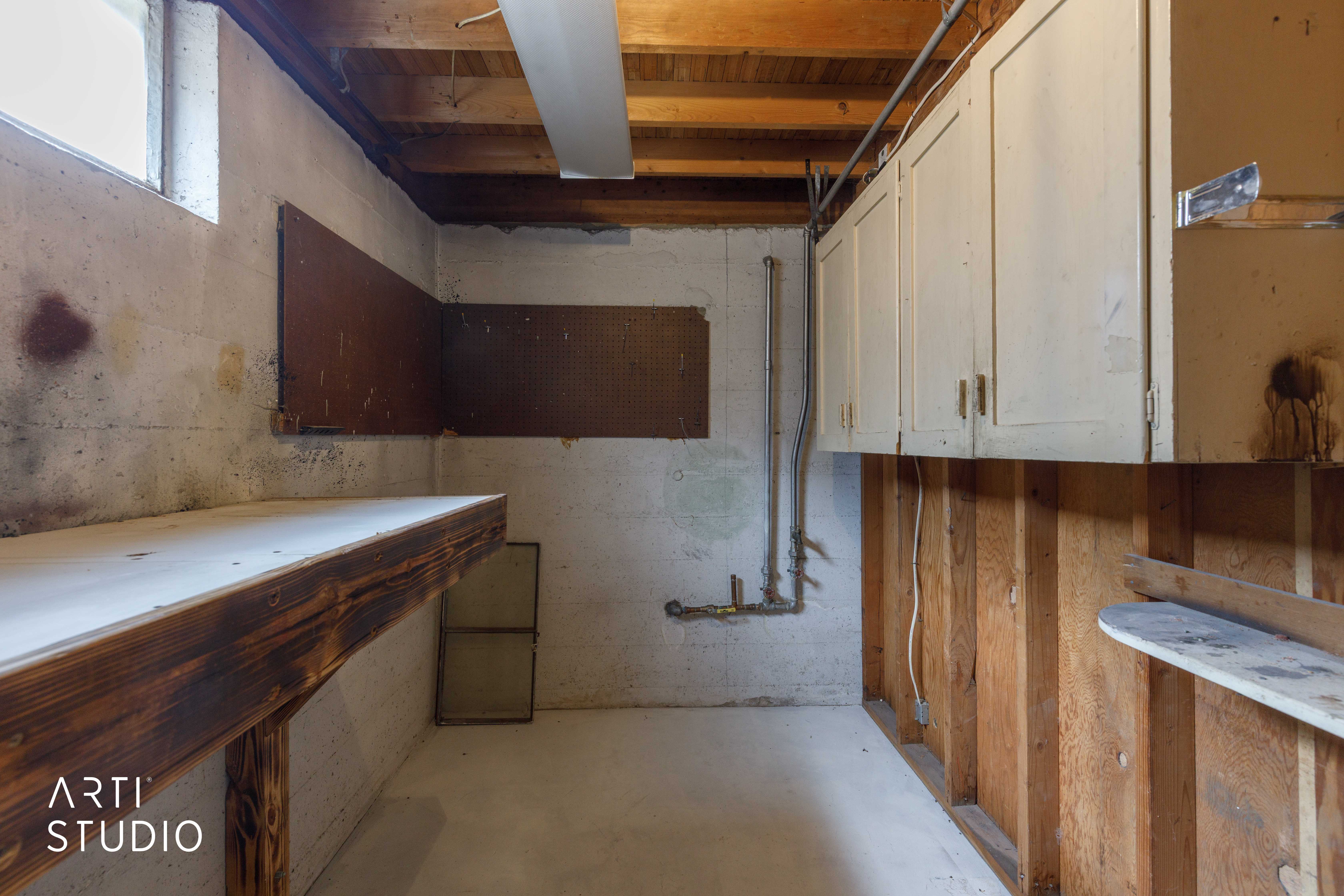 Utility space featuring exposed wood ceiling joists, a built-in workbench, a window, wall-mounted cabinetry, and exposed wall studs