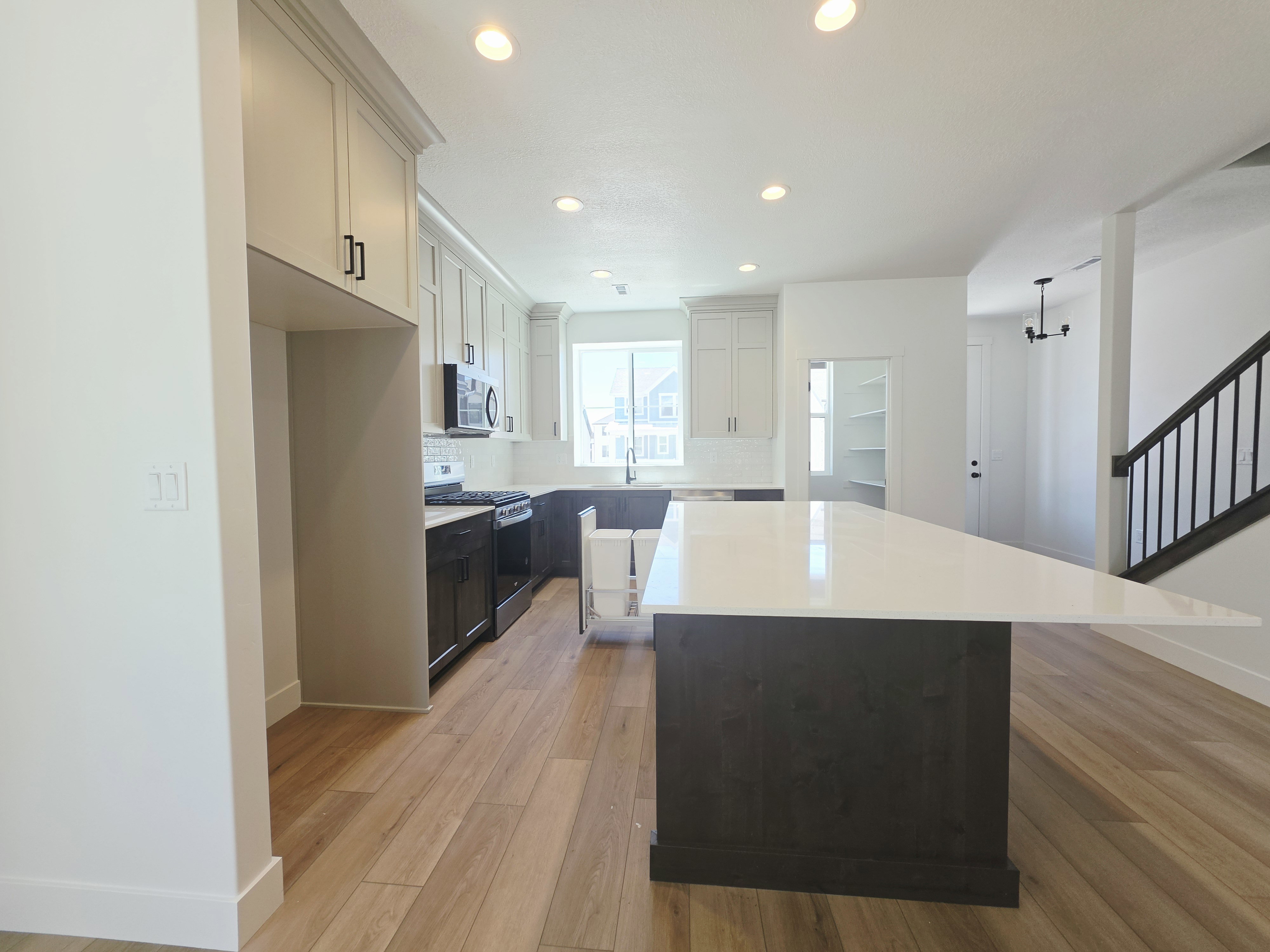 Kitchen featuring a large central island with a white countertop and dark wood-finish cabinetry, wood-finish flooring, recessed lighting, and a pantry with built-in shelving