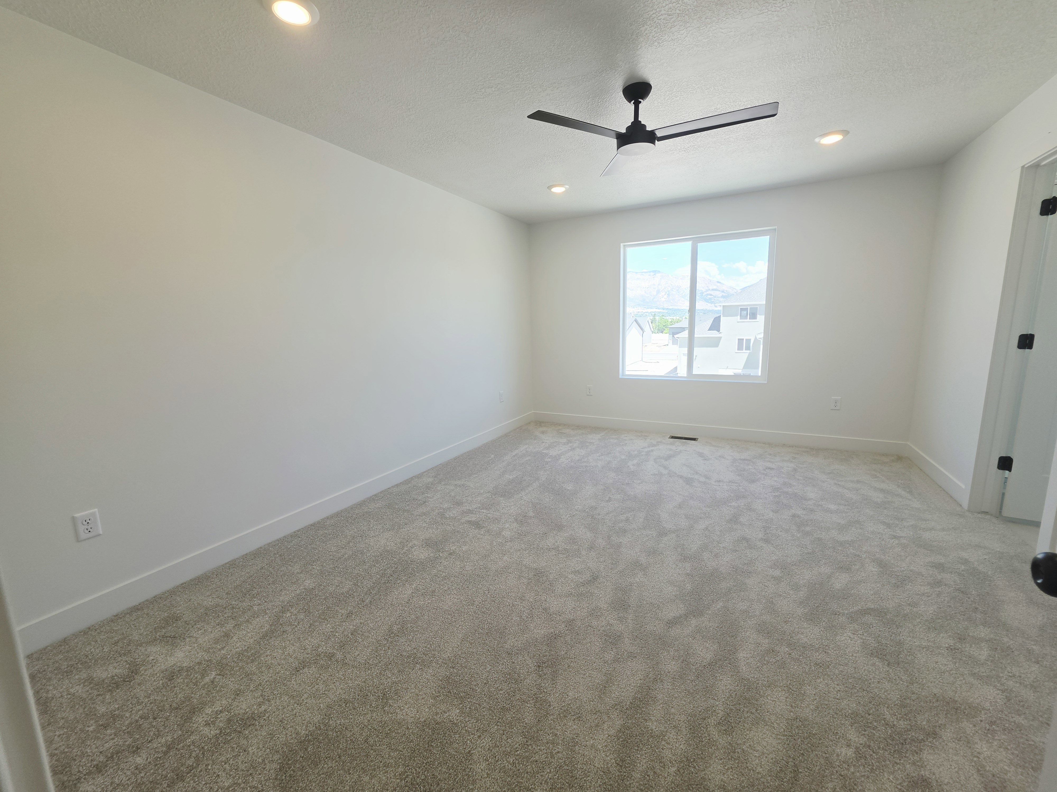 Spacious room featuring neutral carpeting, a large window, a ceiling fan with integrated lighting, and recessed ceiling lights