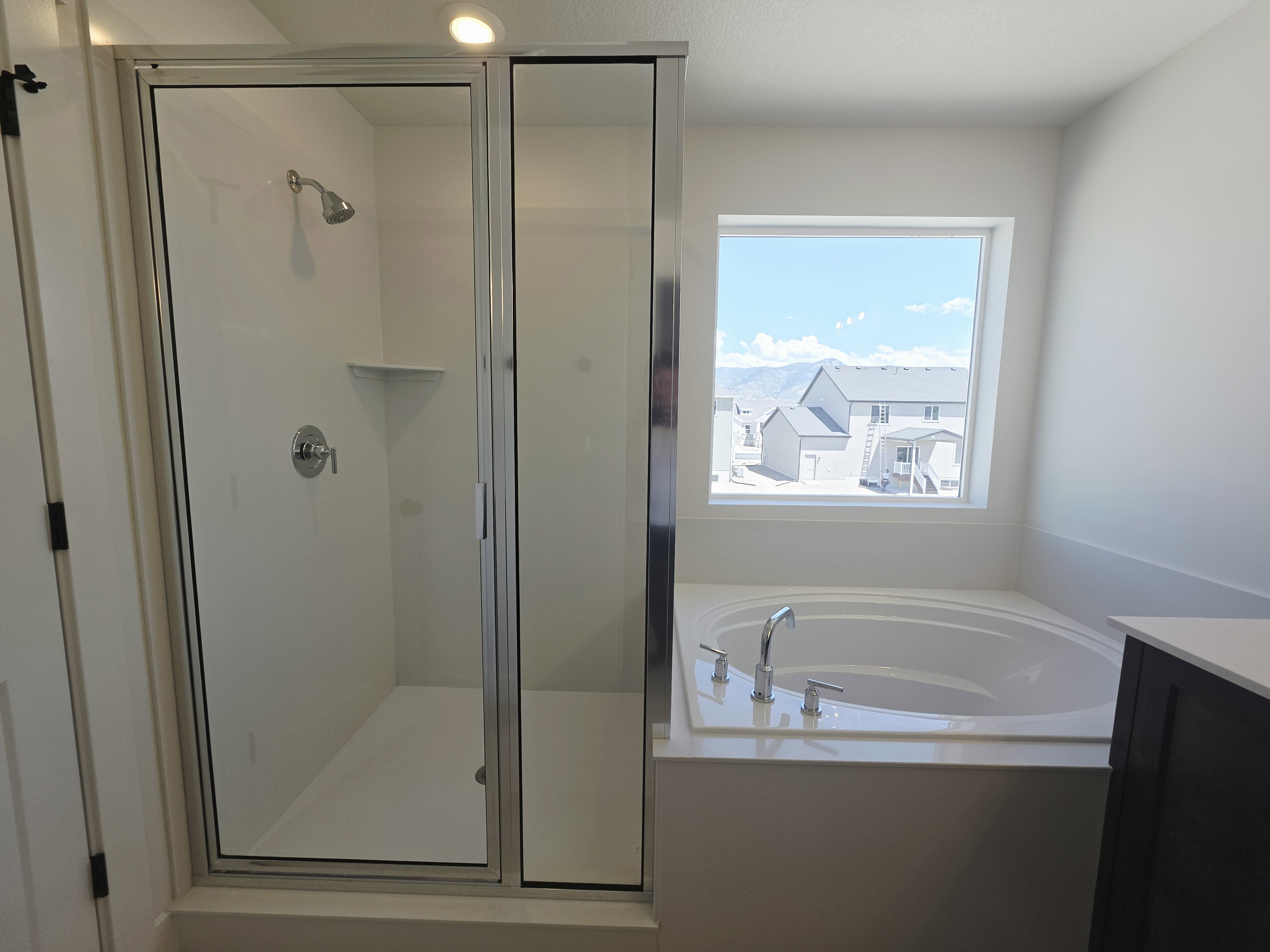 Spacious bathroom featuring a glass-enclosed shower with chrome fixtures, a built-in corner shelf, and a large soaking tub with chrome faucet