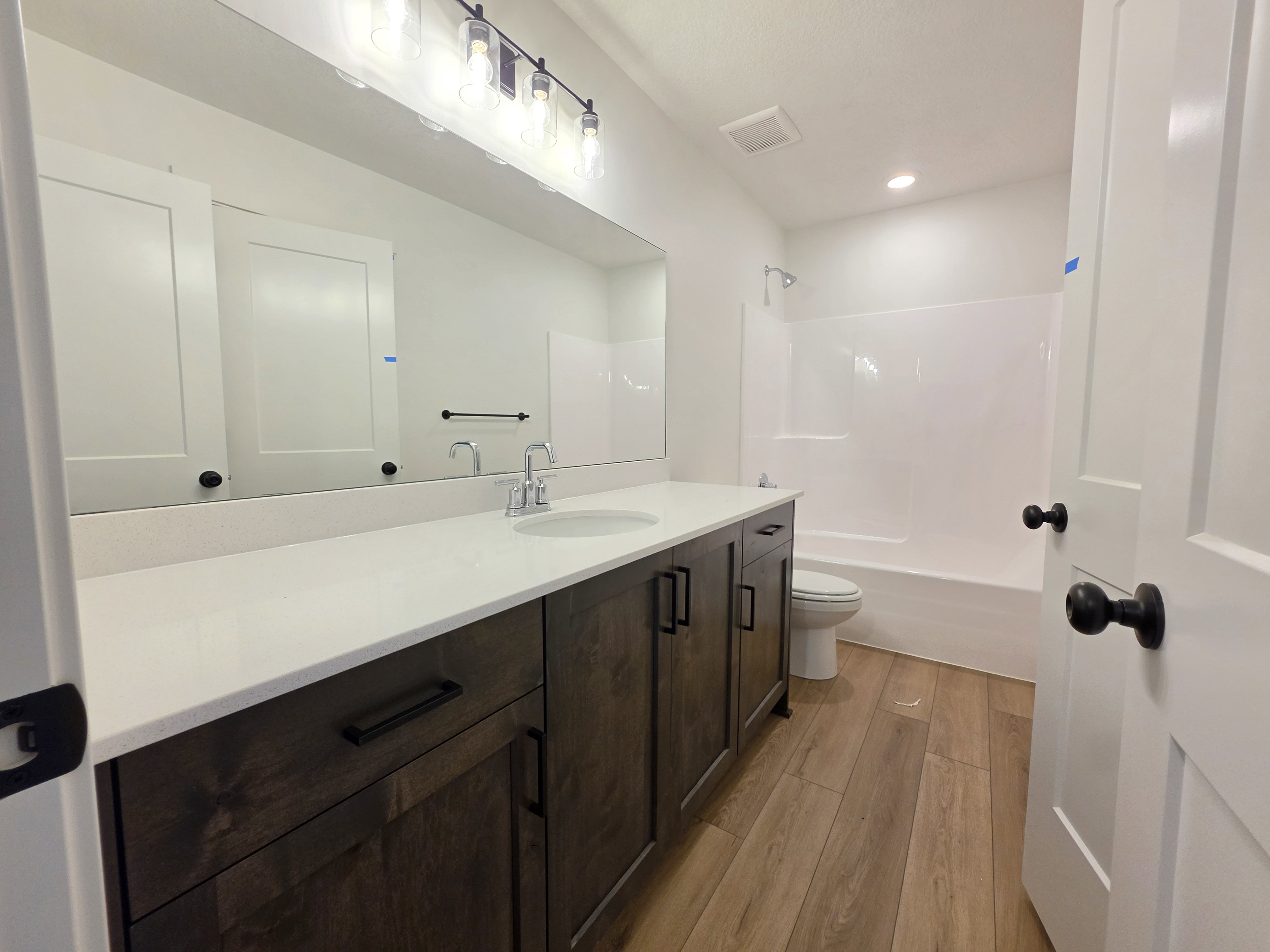 Bathroom featuring a wood-finish floor, a dark wood-finish vanity with a light-toned countertop, a rectangular undermount sink, and a built-in shower/tub combination
