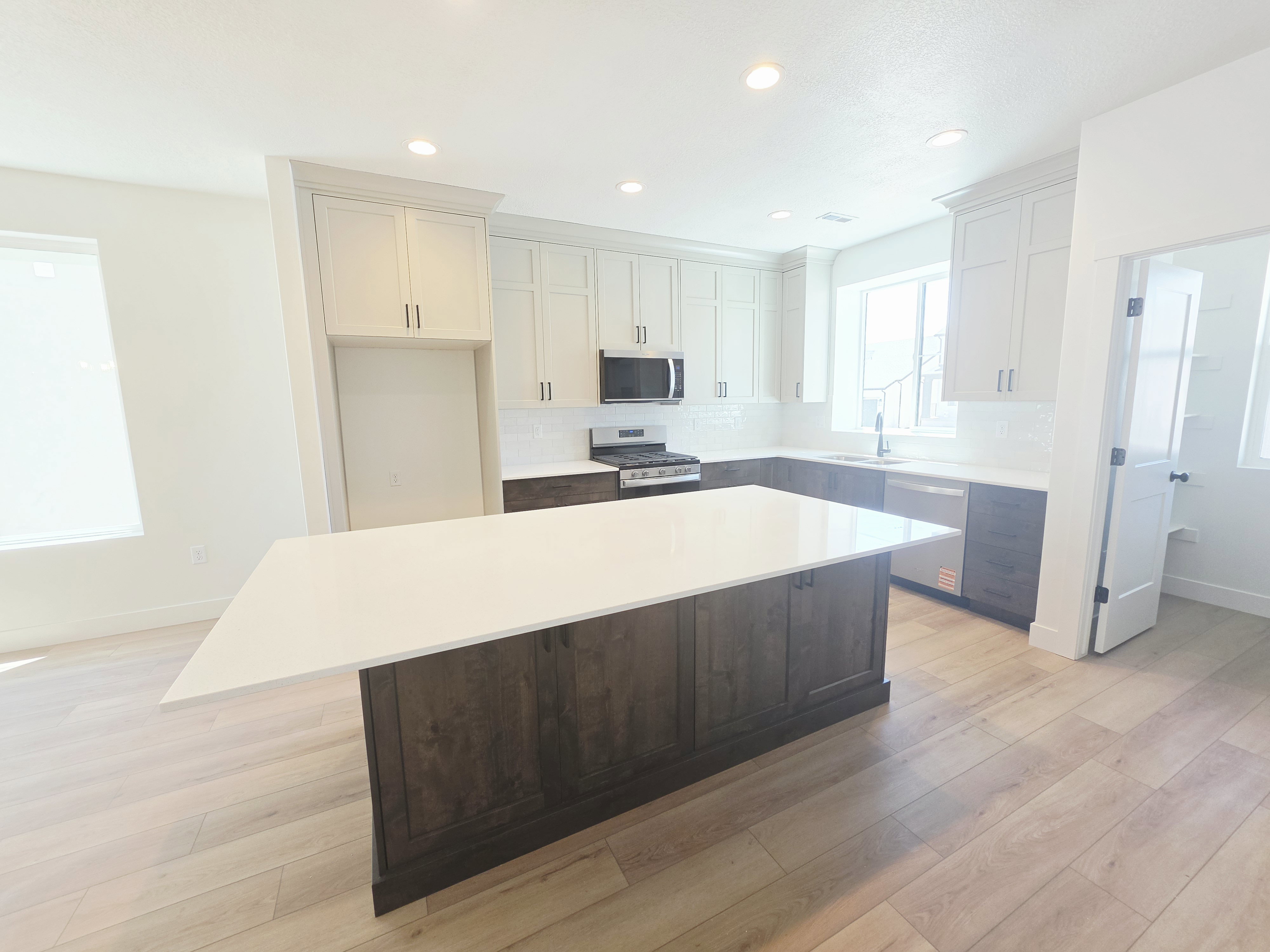 Spacious kitchen featuring a large island with a white countertop, two-tone cabinetry, stainless steel appliances, and wood-finish flooring