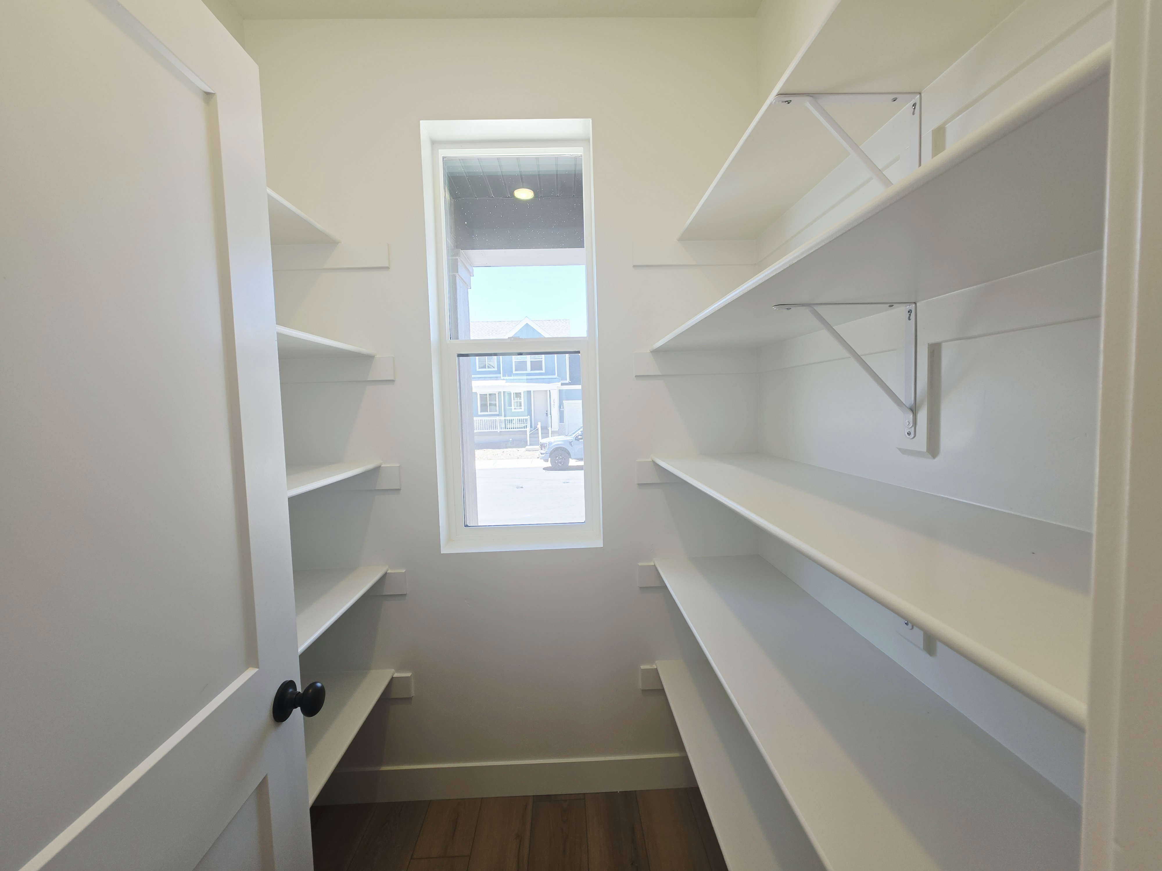 Pantry featuring extensive built-in shelving, a single window, and wood-finish flooring