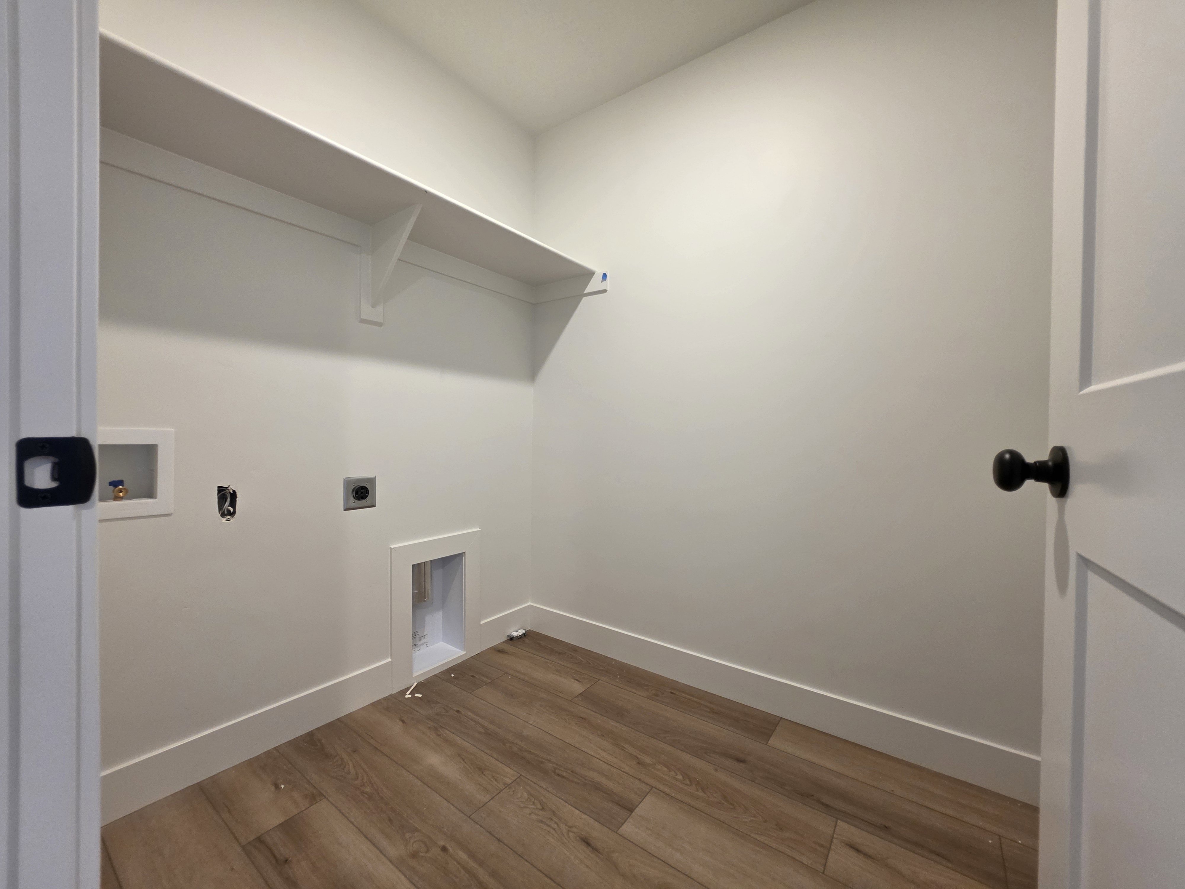 Dedicated laundry space featuring wood-finish flooring, crisp white walls, and a built-in storage shelf