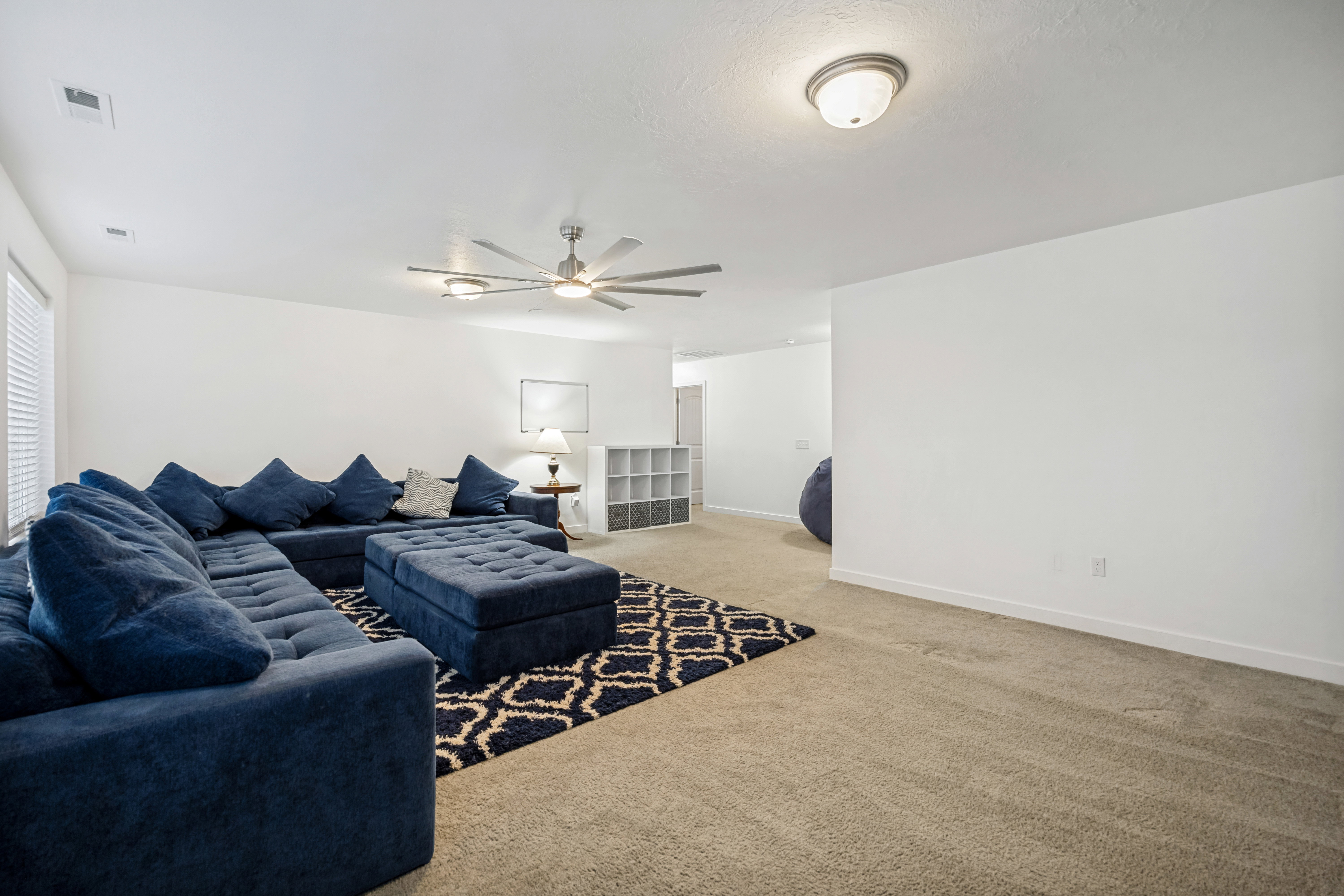 Spacious room featuring neutral carpeting, white walls, a ceiling fan with integrated lighting, and a recessed ceiling light fixture