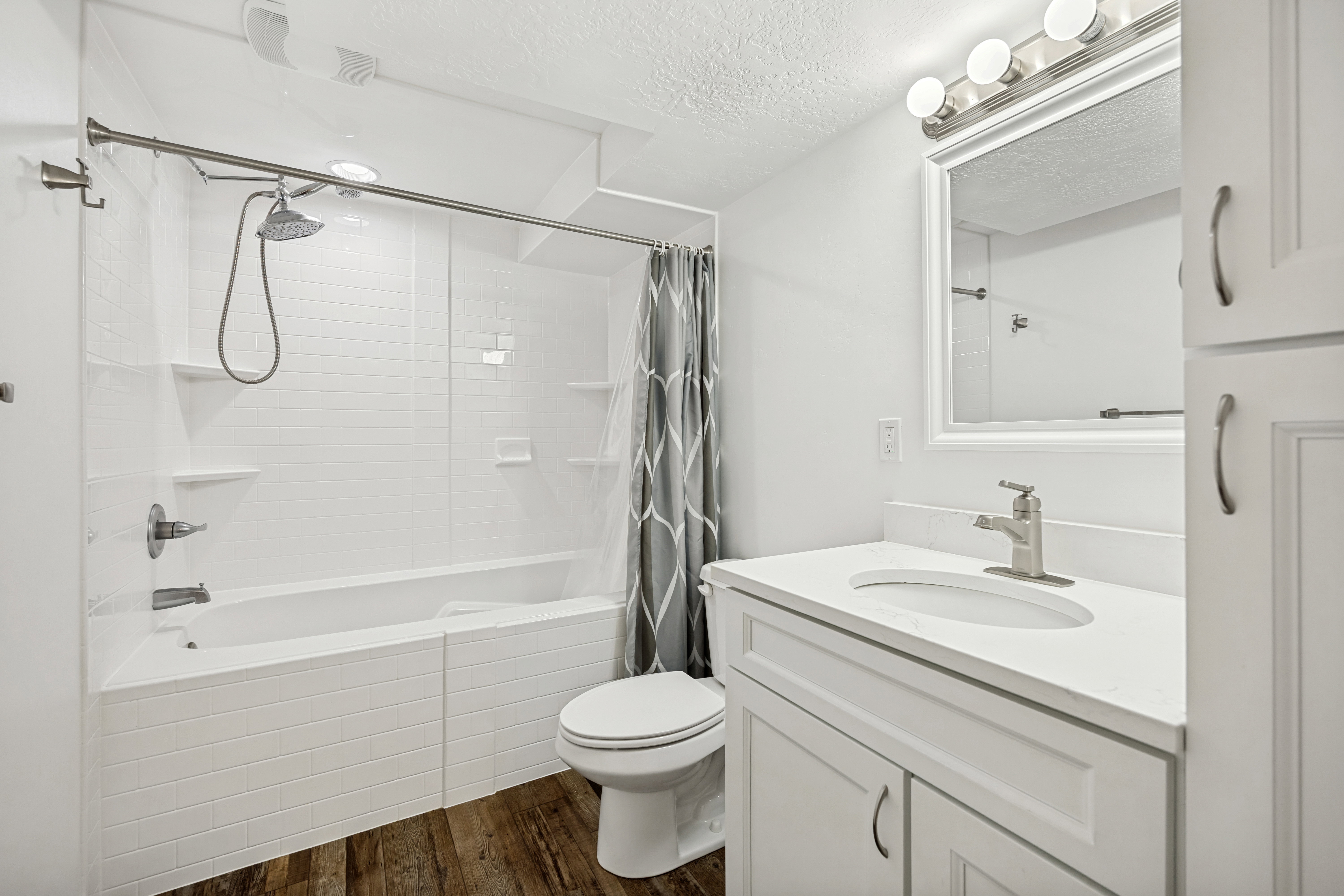 Bathroom featuring a white subway tile tub surround, white vanity with integrated sink, white countertop, and wood-finish flooring