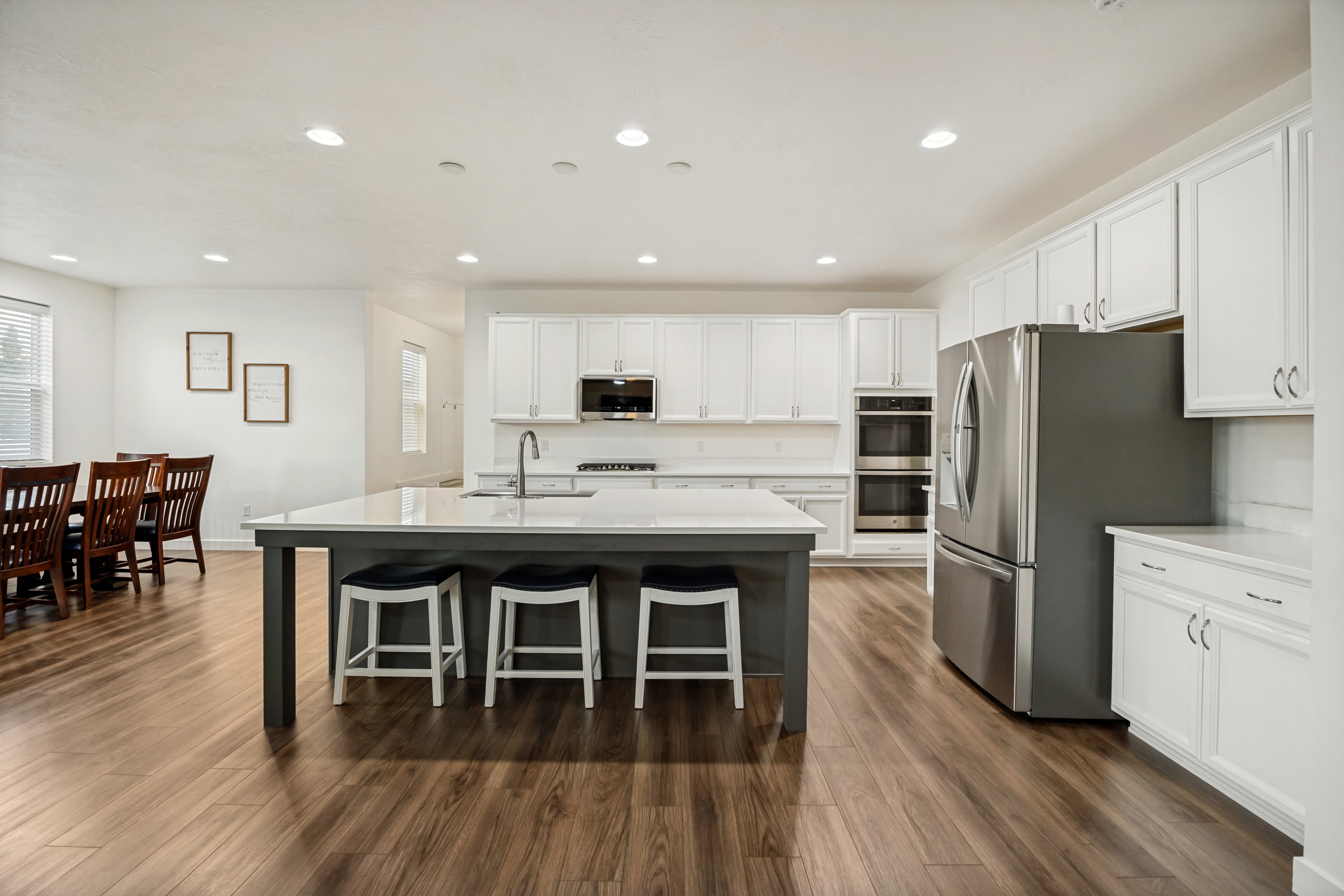 Open-concept kitchen featuring an island with seating, white shaker cabinetry, stainless steel appliances including a double oven and refrigerator, and wood-finish flooring