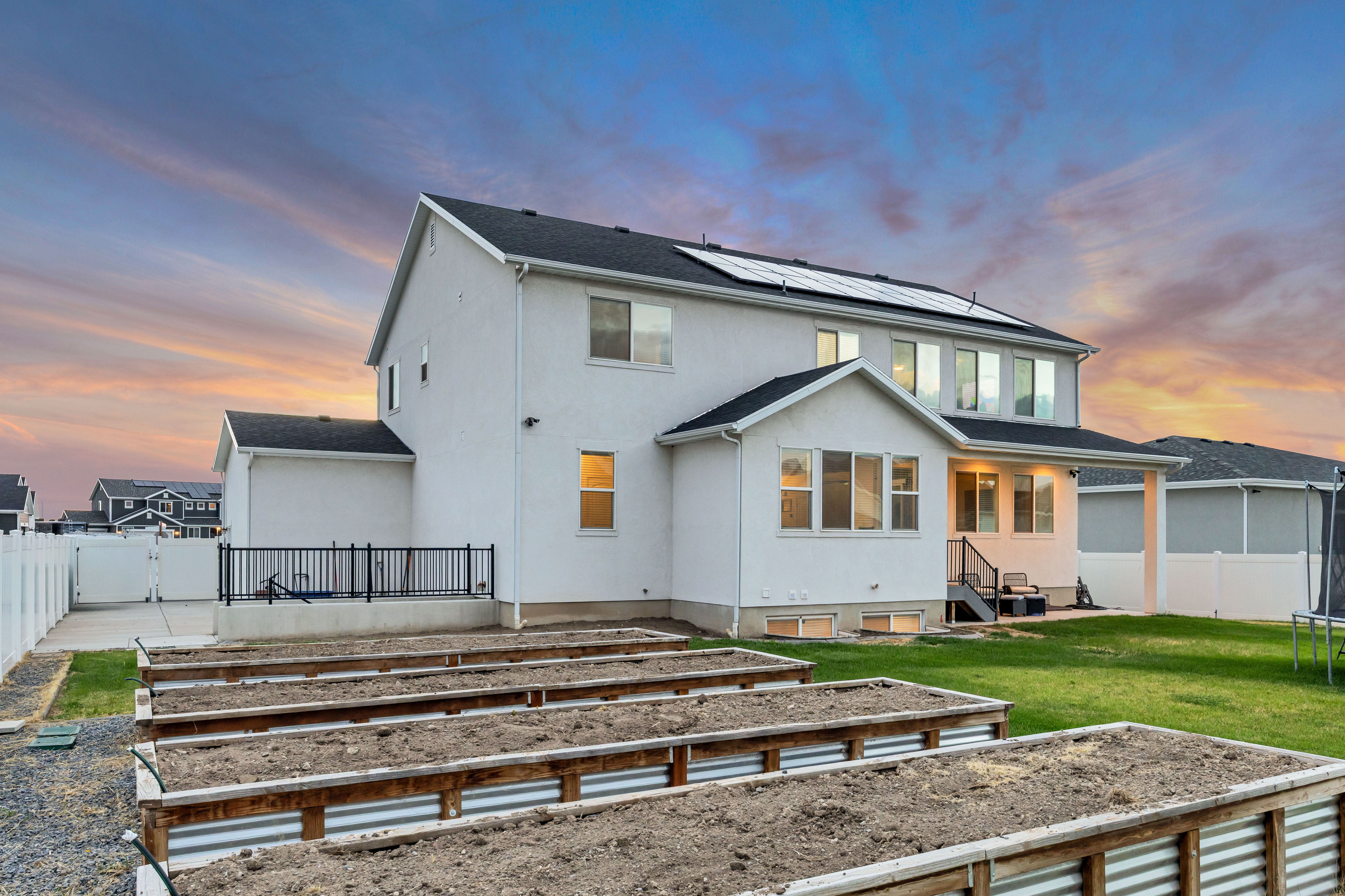 White stucco exterior featuring a tiered backyard with multiple raised garden beds, a grass lawn, and a concrete patio