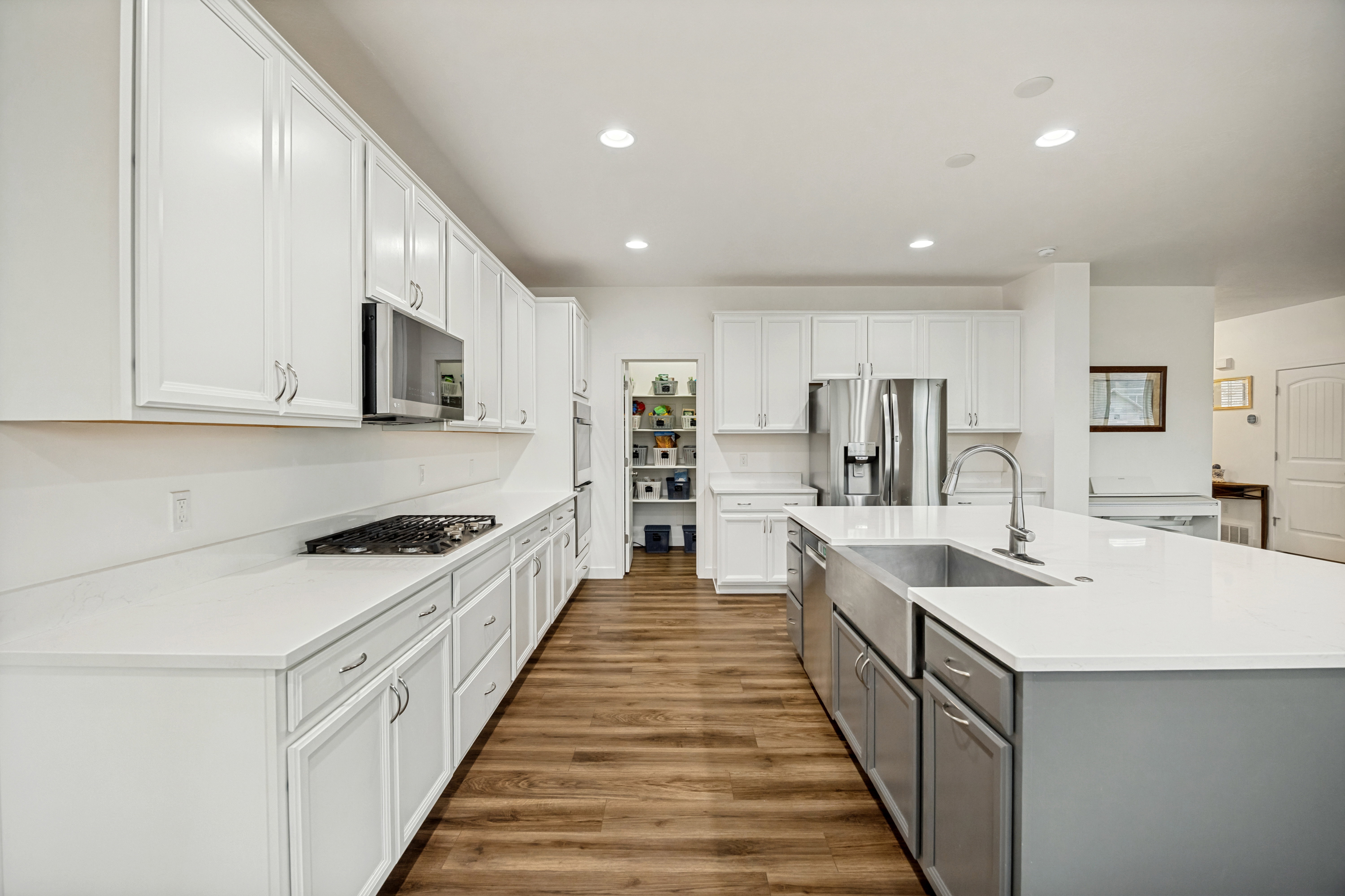 Modern kitchen featuring white cabinetry, light countertops, wood-finish flooring, a central island with a farmhouse sink, and a built-in gas range