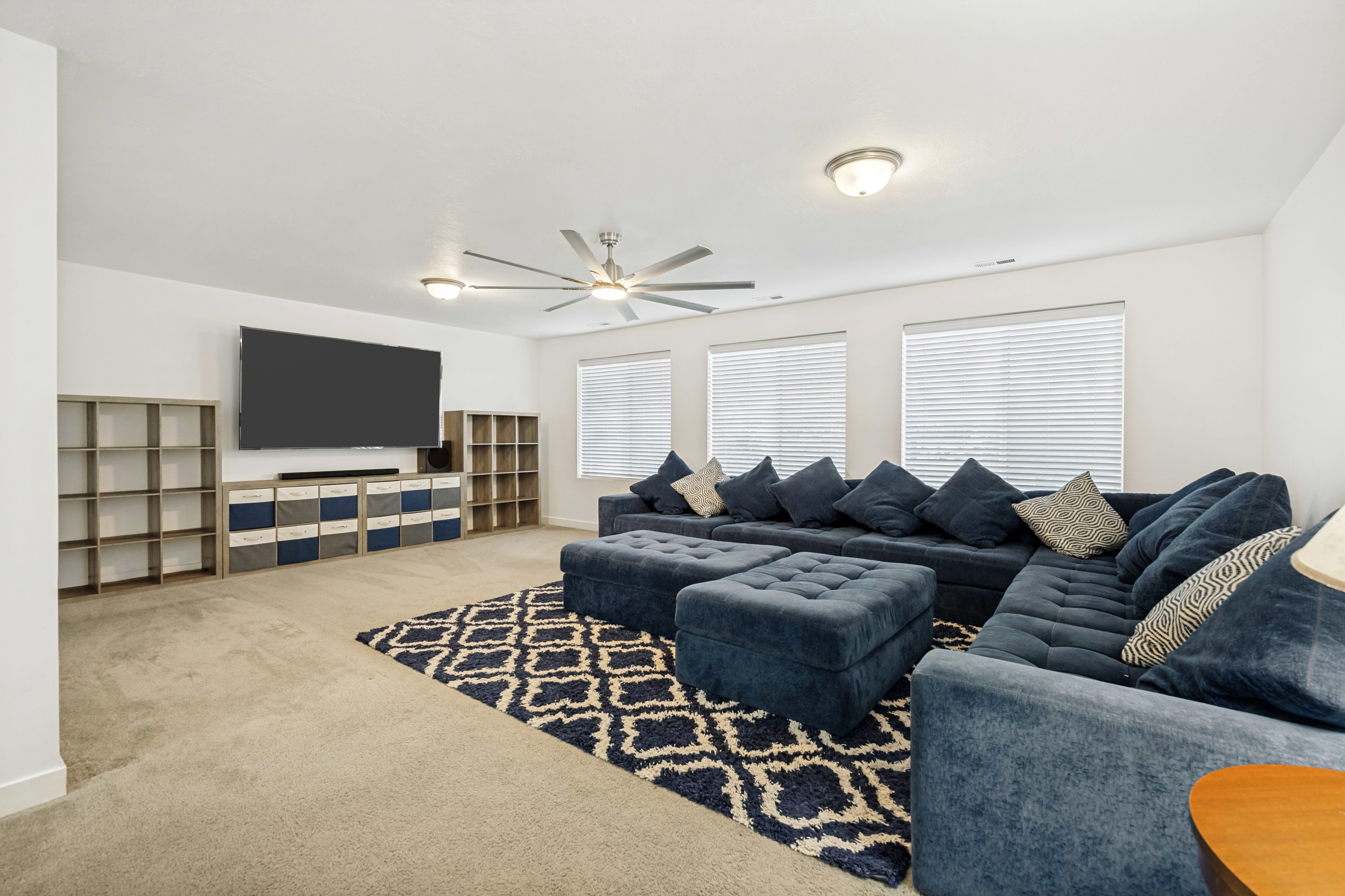 Spacious room featuring light-colored carpeting, a ceiling fan with integrated lighting, and multiple windows with blinds