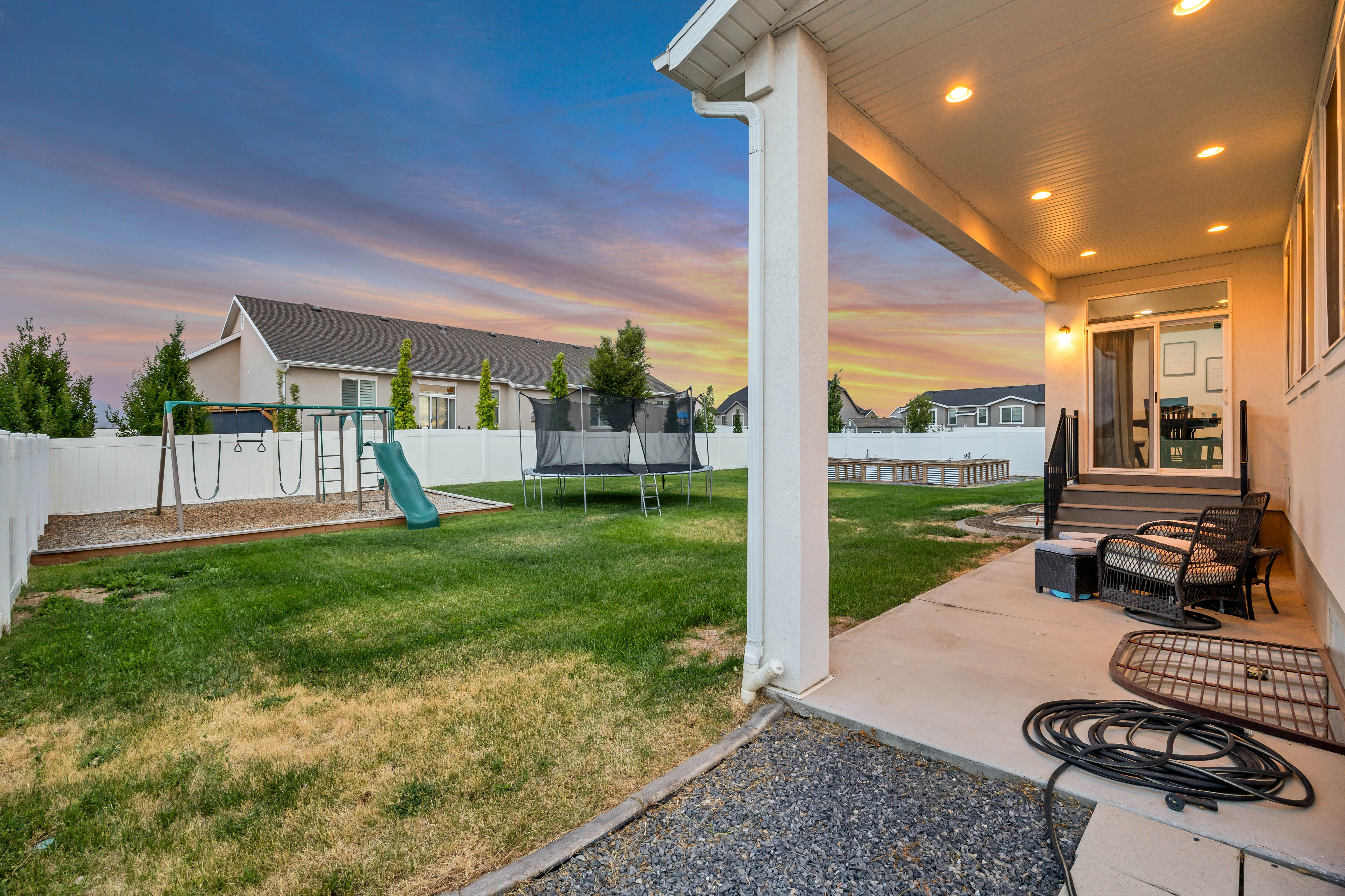Expansive backyard featuring a white vinyl fence, a concrete patio, and a covered porch with recessed lighting