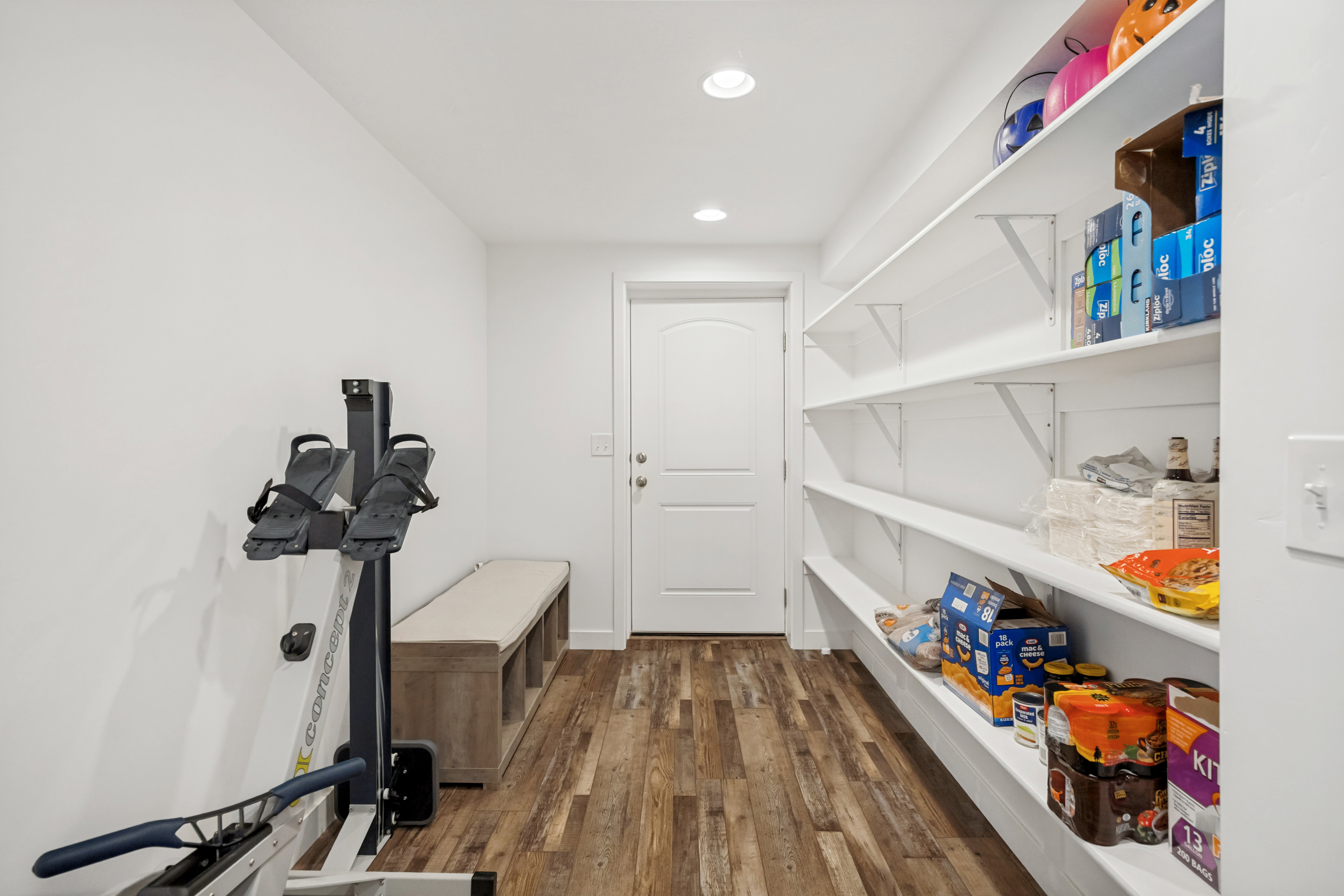 Dedicated storage room featuring extensive built-in shelving, wood-finish flooring, recessed lighting, and a white paneled door