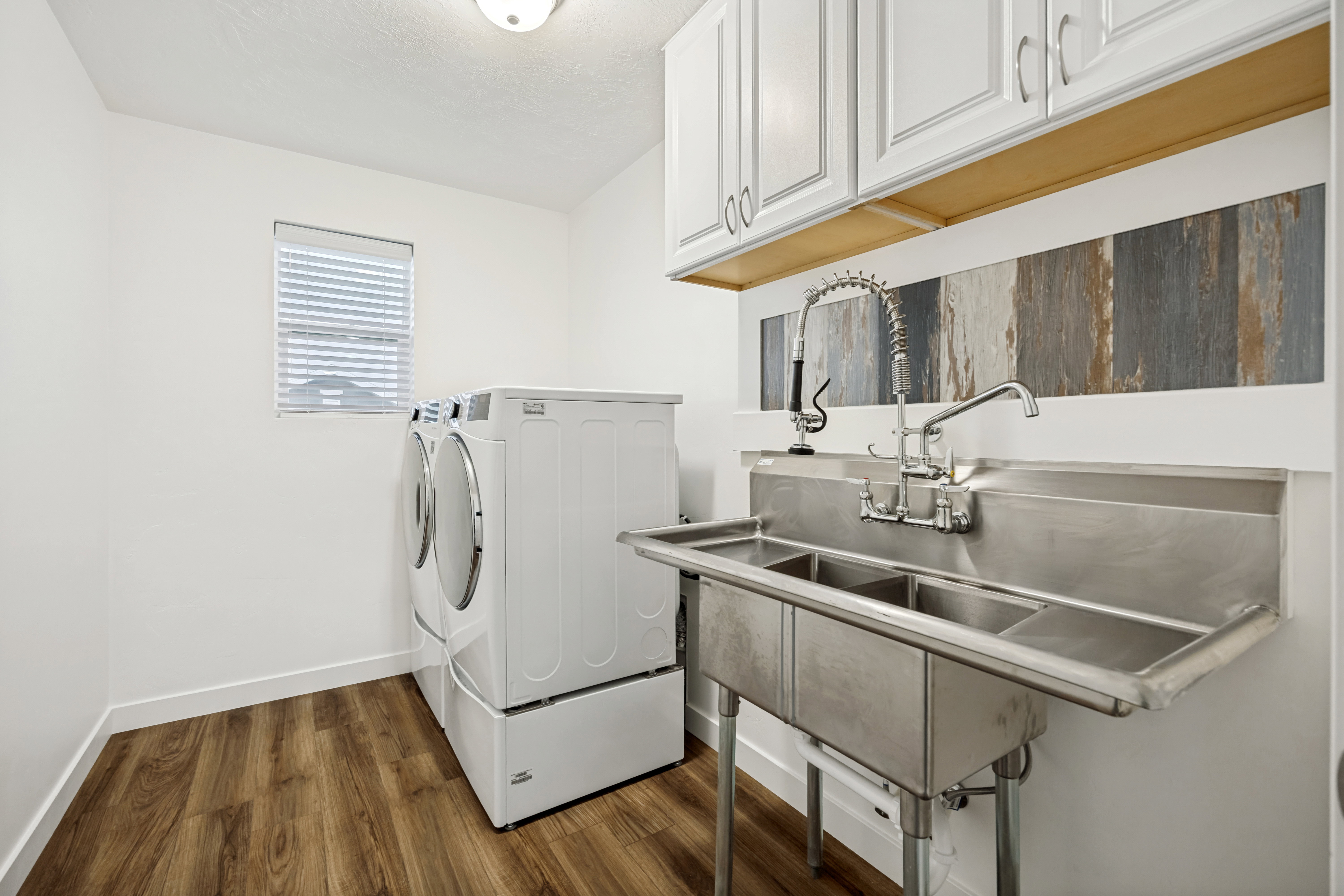 Laundry room featuring wood-finish flooring, a utility sink with dual faucets, and upper cabinetry