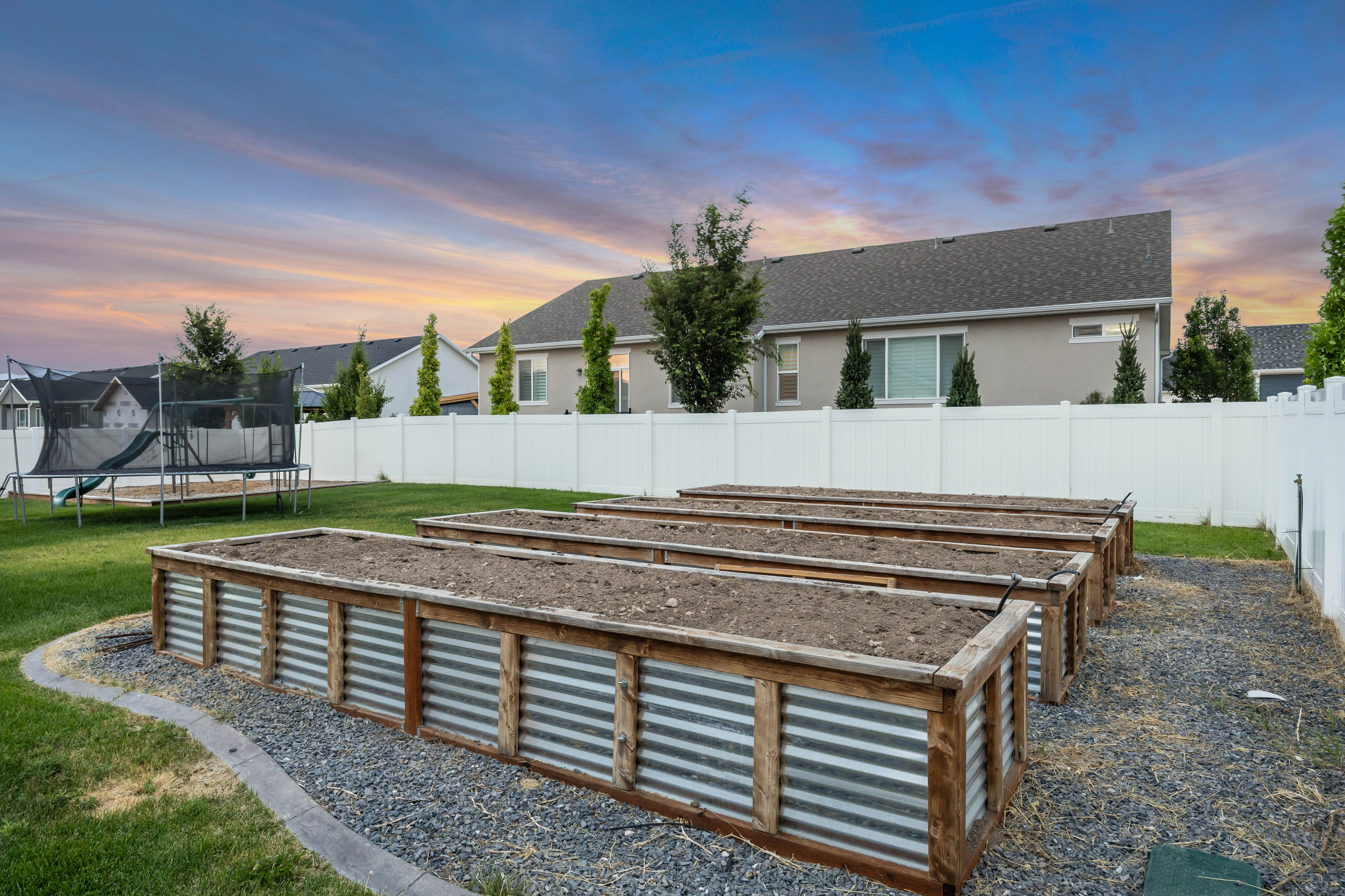 Backyard featuring multiple raised garden beds with wood and corrugated metal construction, surrounded by pea gravel