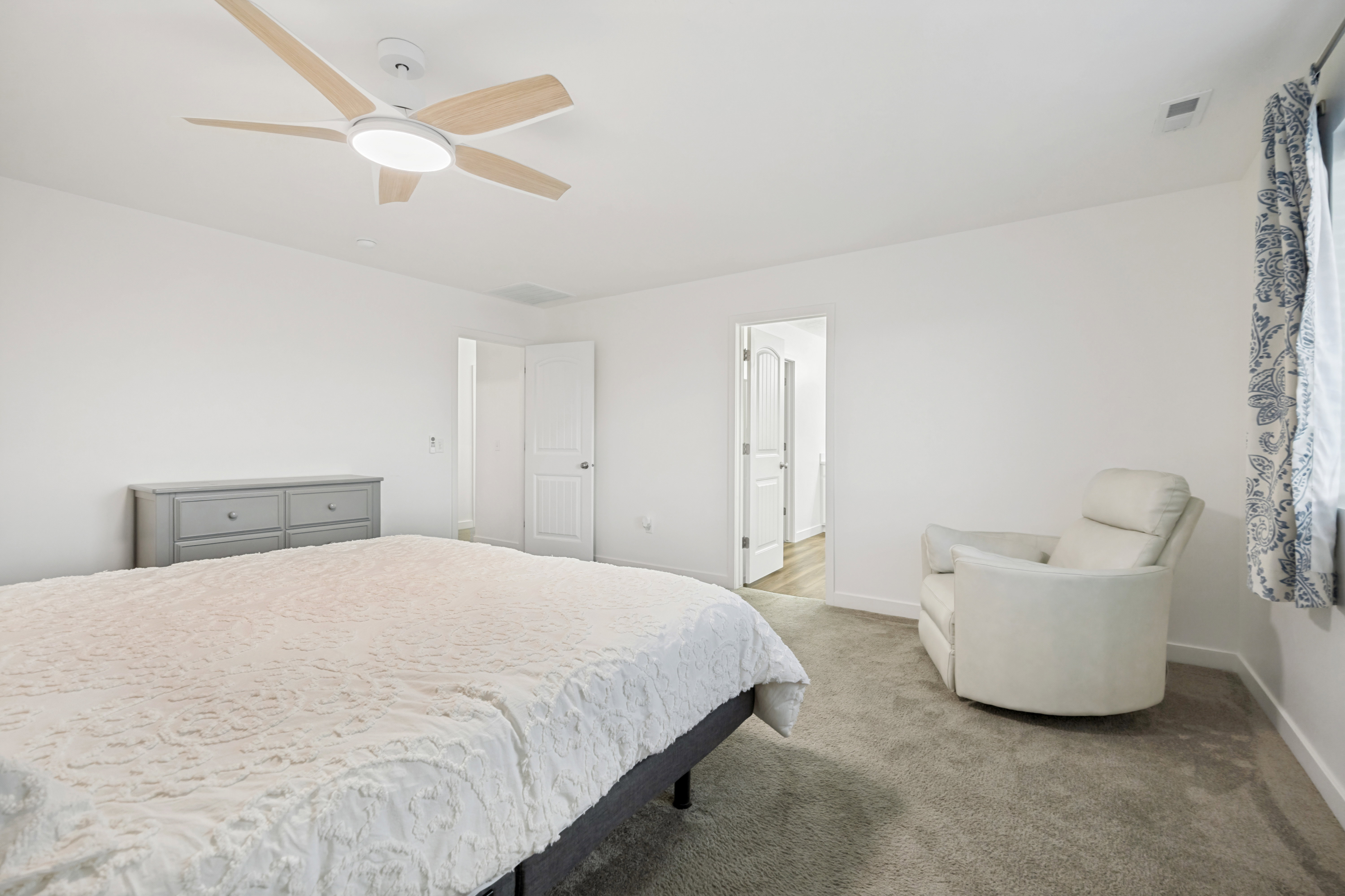 Carpeted bedroom featuring a modern ceiling fan with light fixture, white walls, and a window with patterned curtains