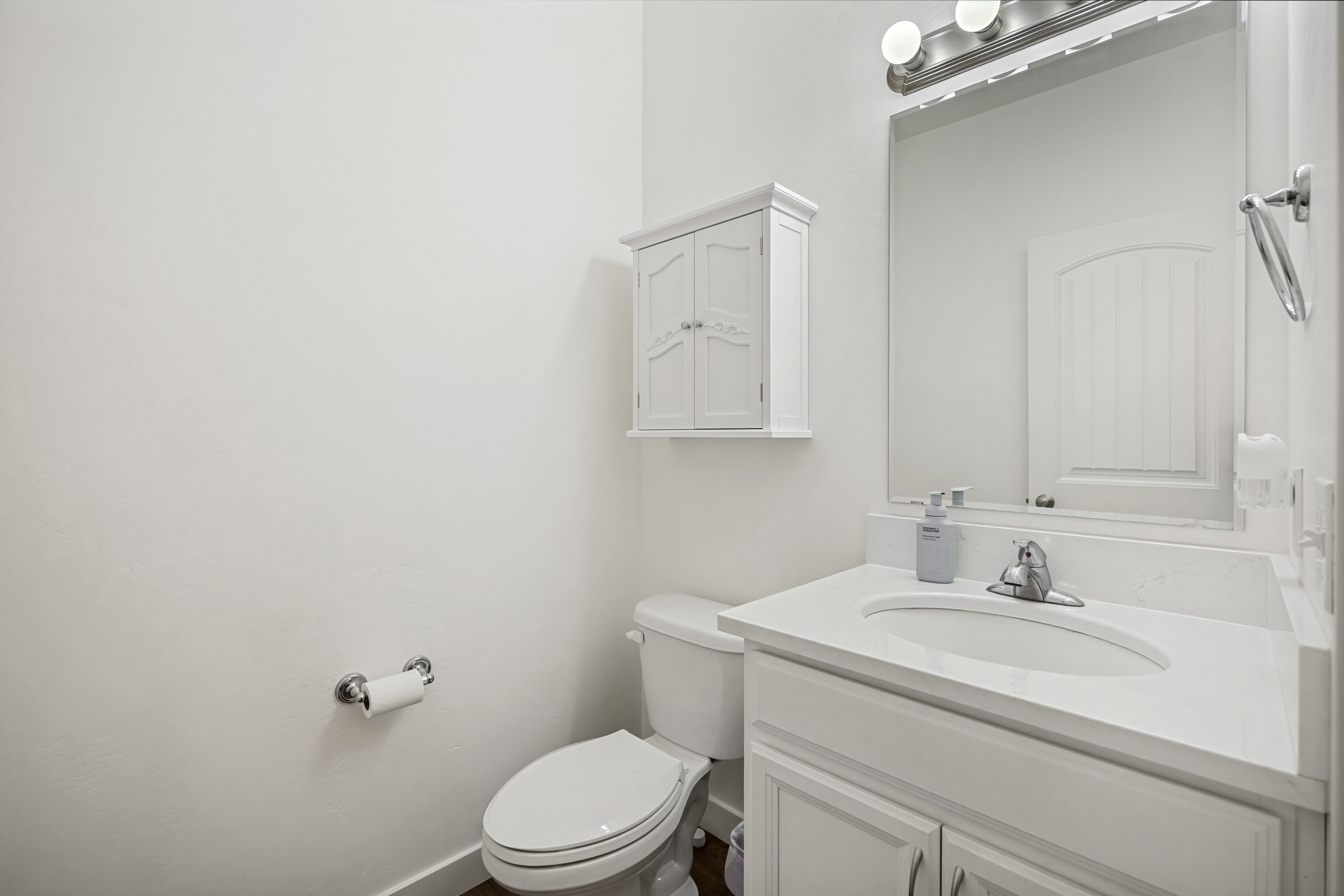 Bathroom featuring a white vanity with an integrated sink and countertop, chrome faucet, and a wall-mounted mirror with a three-bulb light fixture