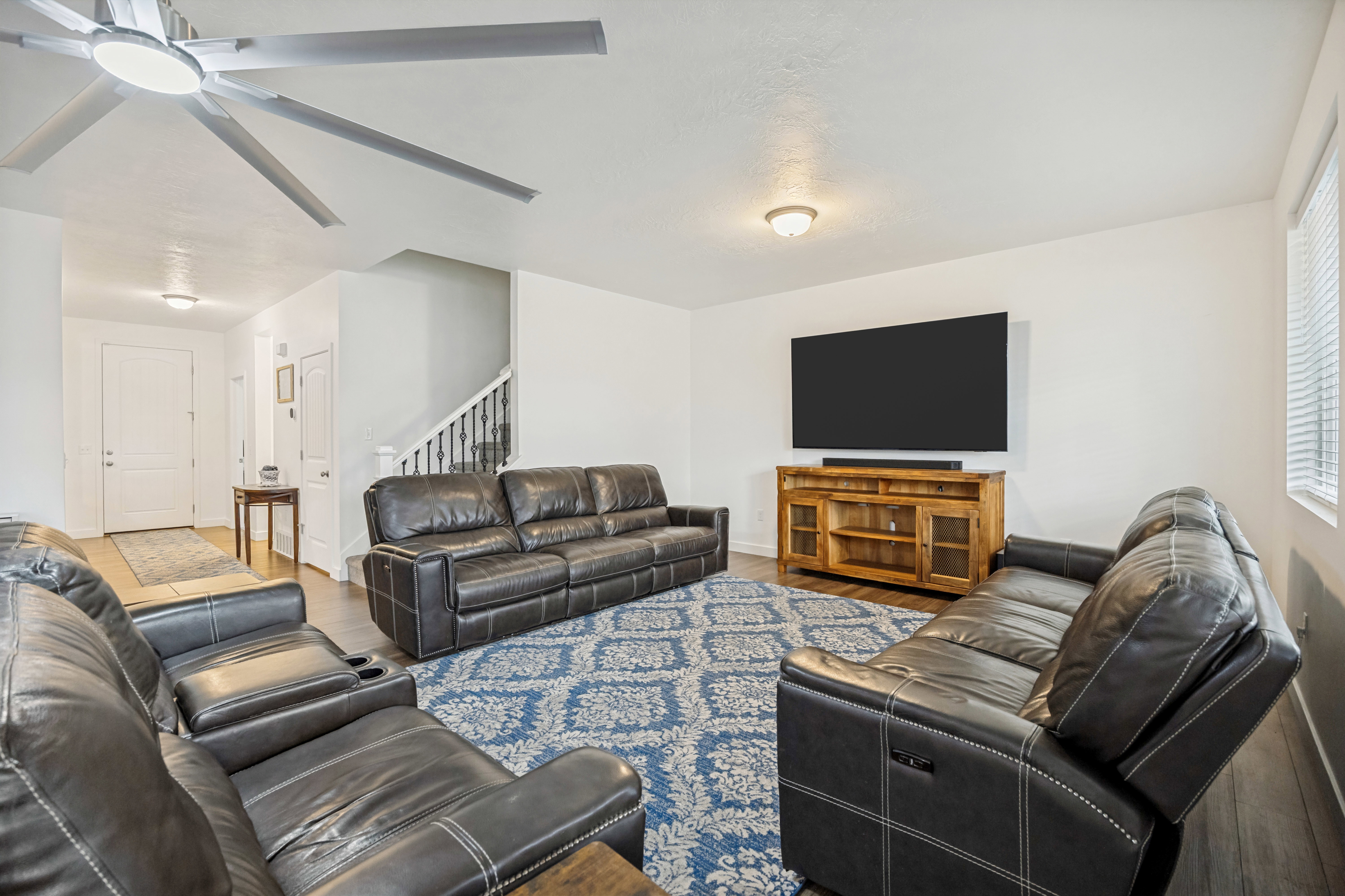 Open-concept living space featuring wood-finish flooring, a large ceiling fan with integrated lighting, and white walls