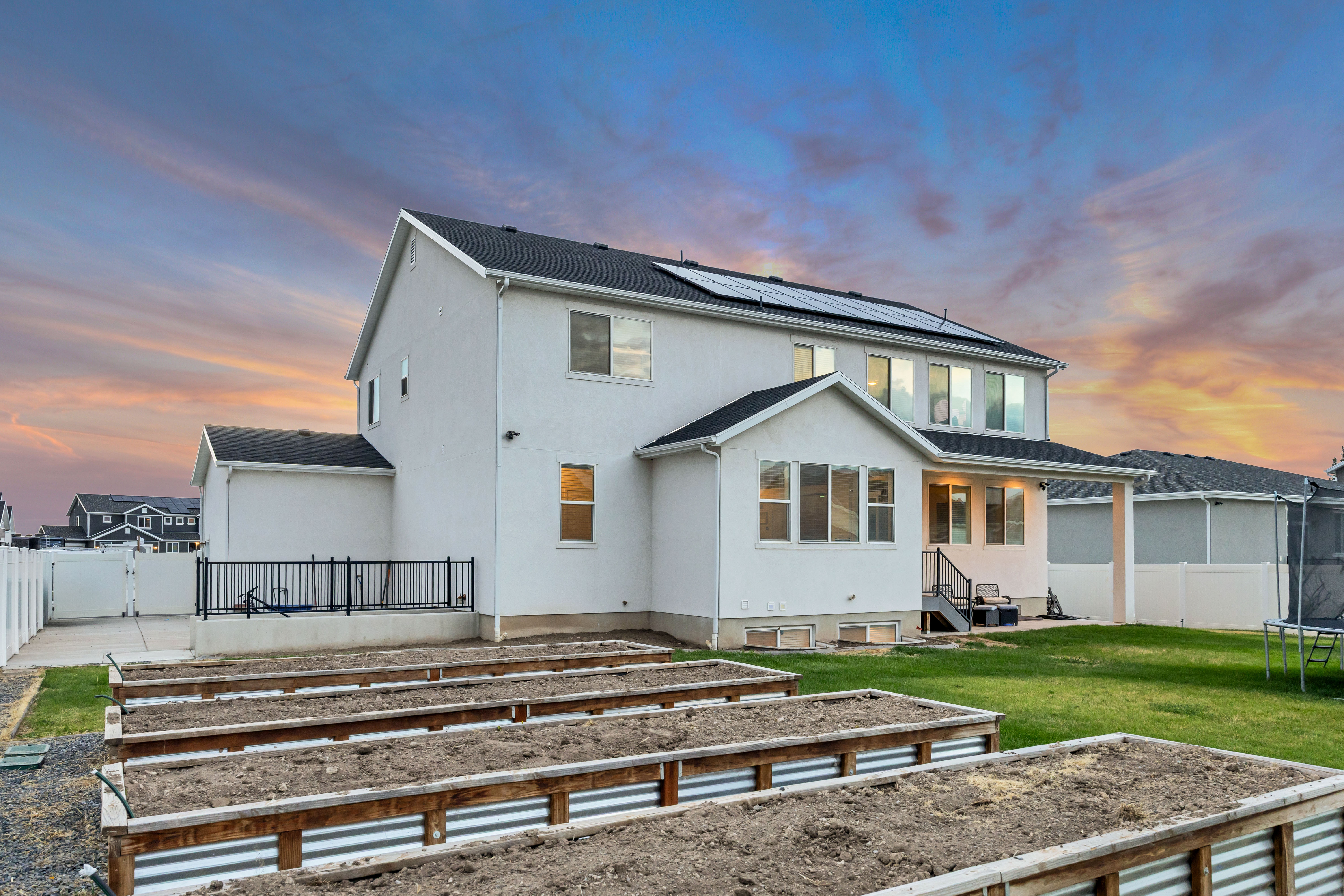 Rear exterior showcasing multiple raised garden beds, a covered patio, and solar panels