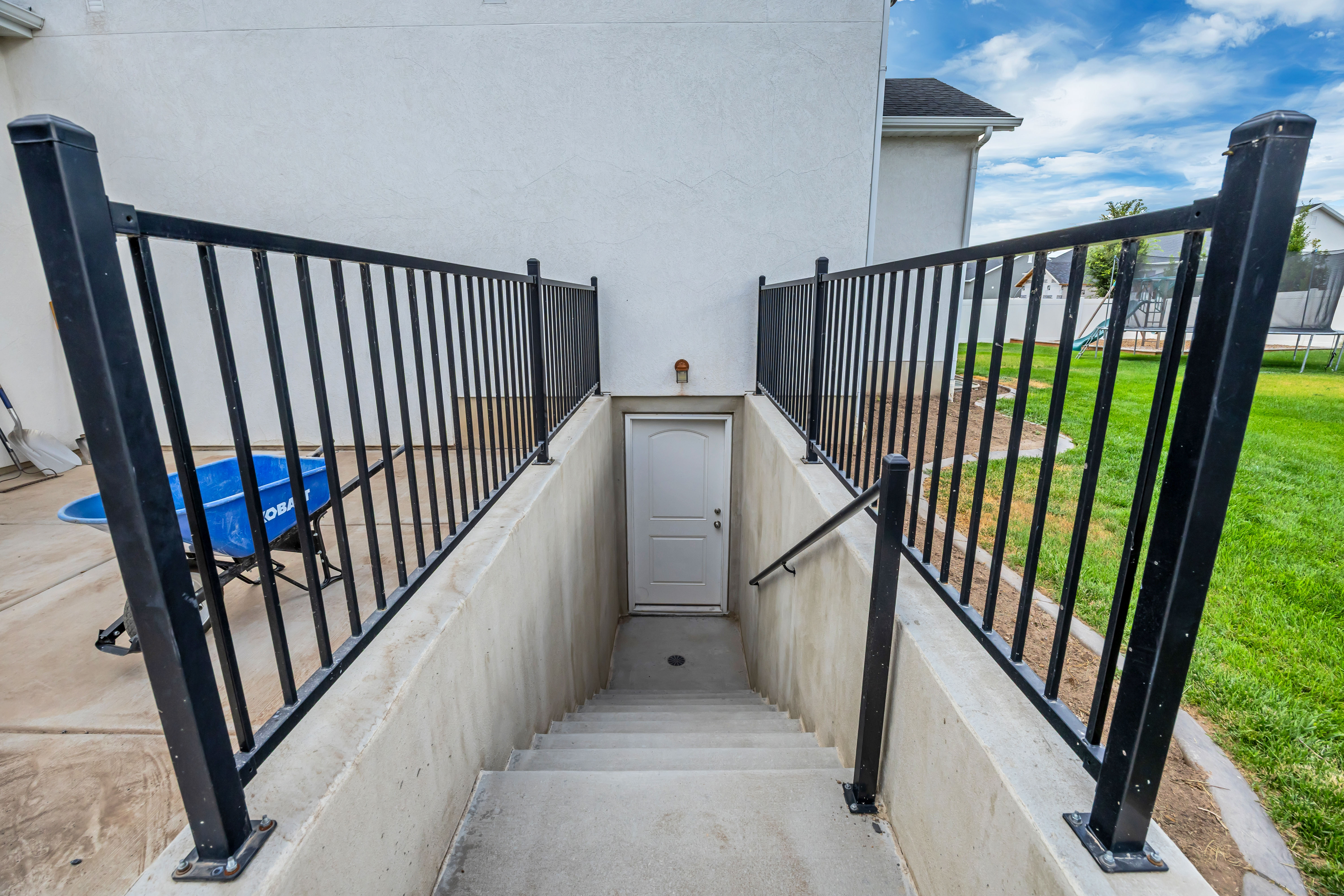 Concrete basement access with a white entry door, sturdy black metal railings, and a concrete handrail