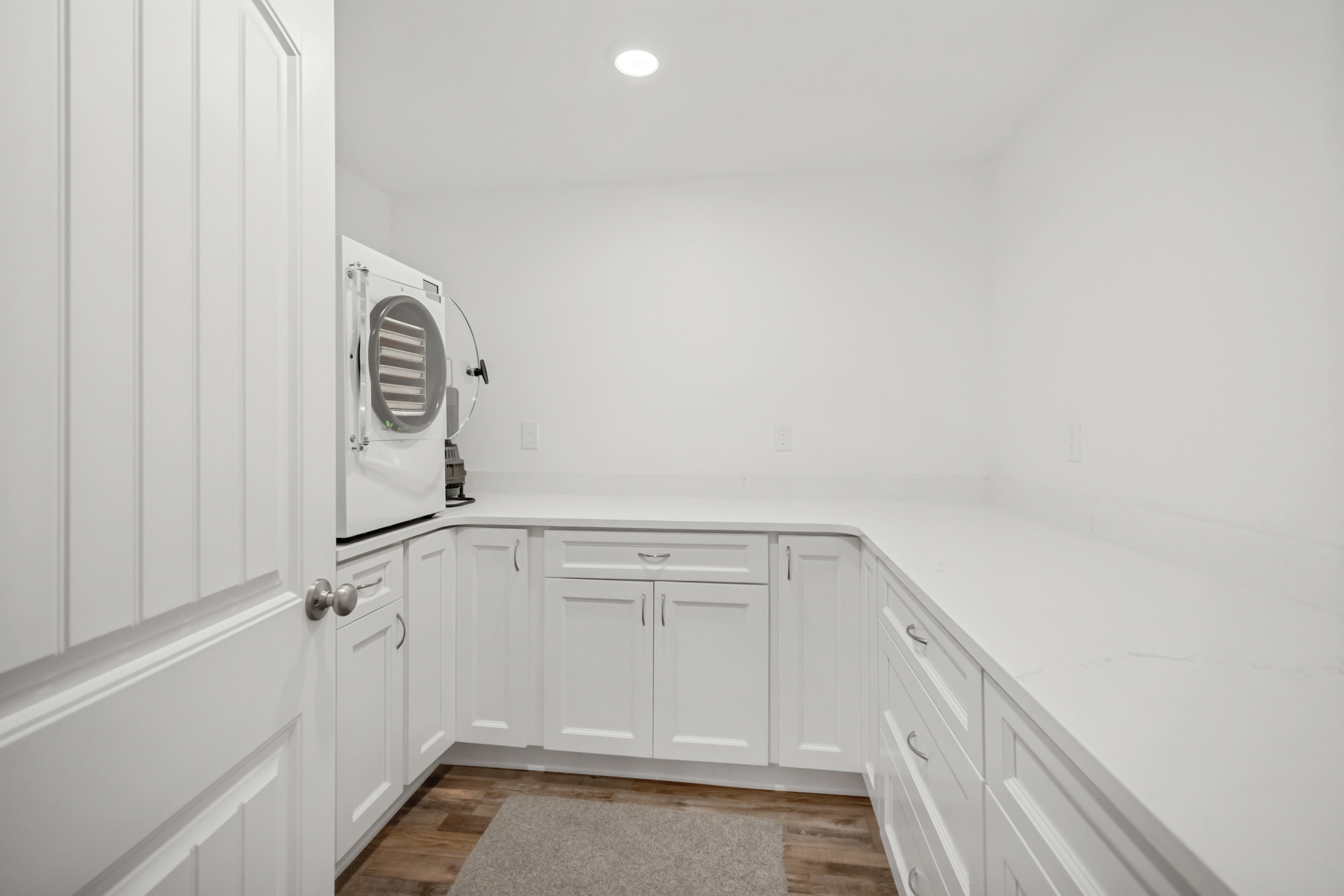 Spacious utility room featuring extensive white cabinetry, light-toned countertops, wood-finish flooring, and recessed ceiling lighting