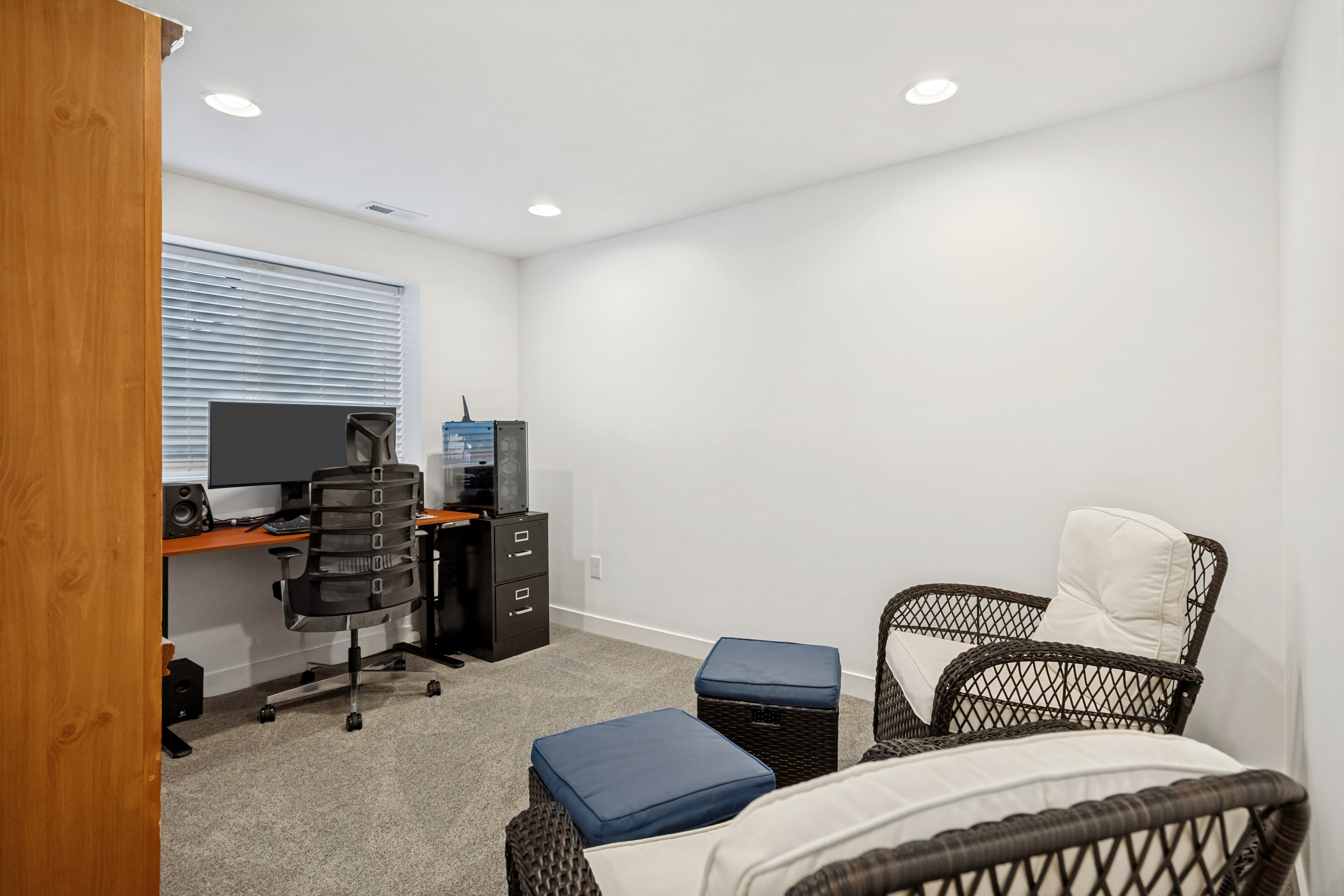 Recessed lighting illuminates a room featuring light gray carpeting, white walls, and a window with horizontal blinds