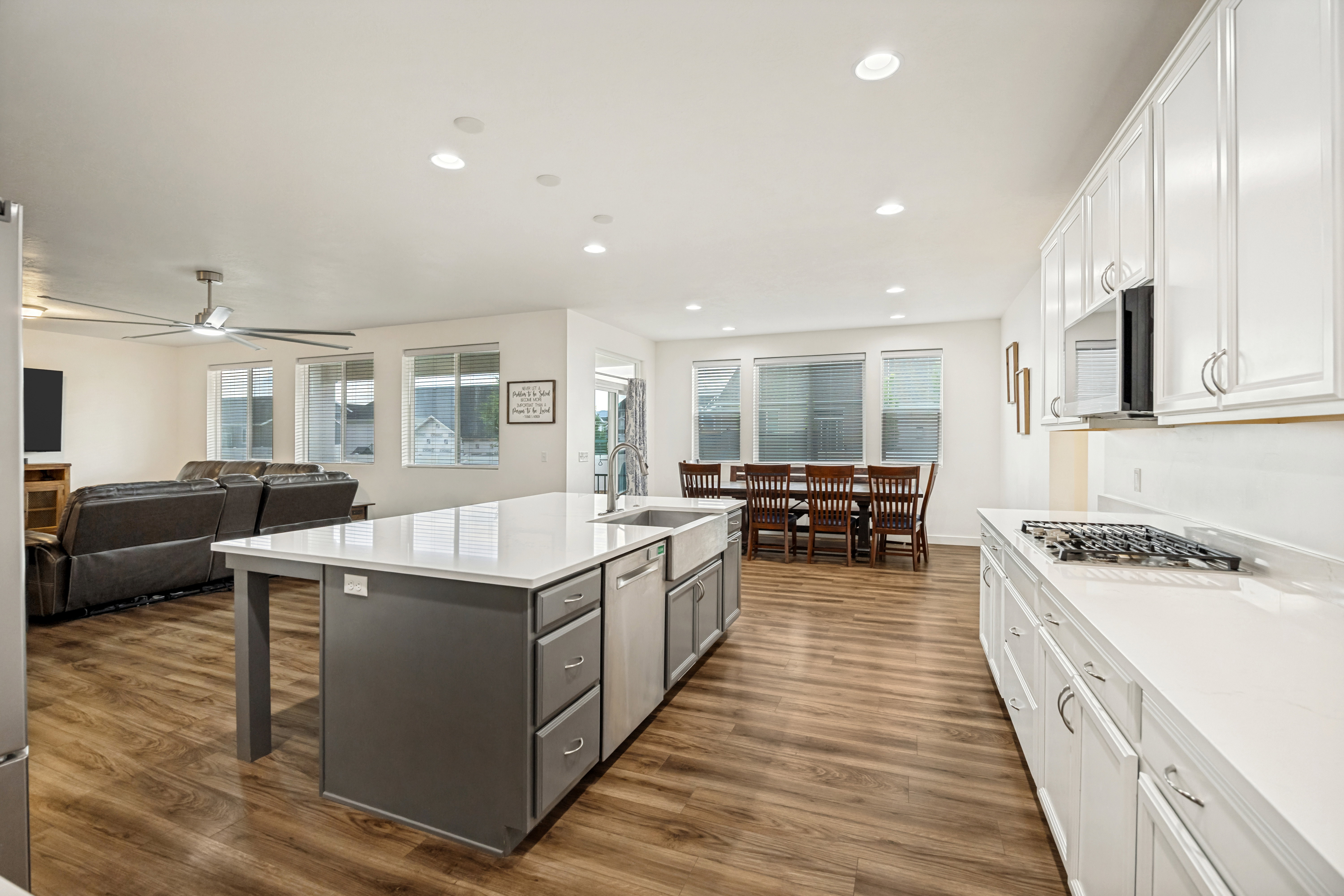 Open-concept kitchen featuring white cabinetry, light countertops, an island with a farmhouse sink, and wood-finish flooring