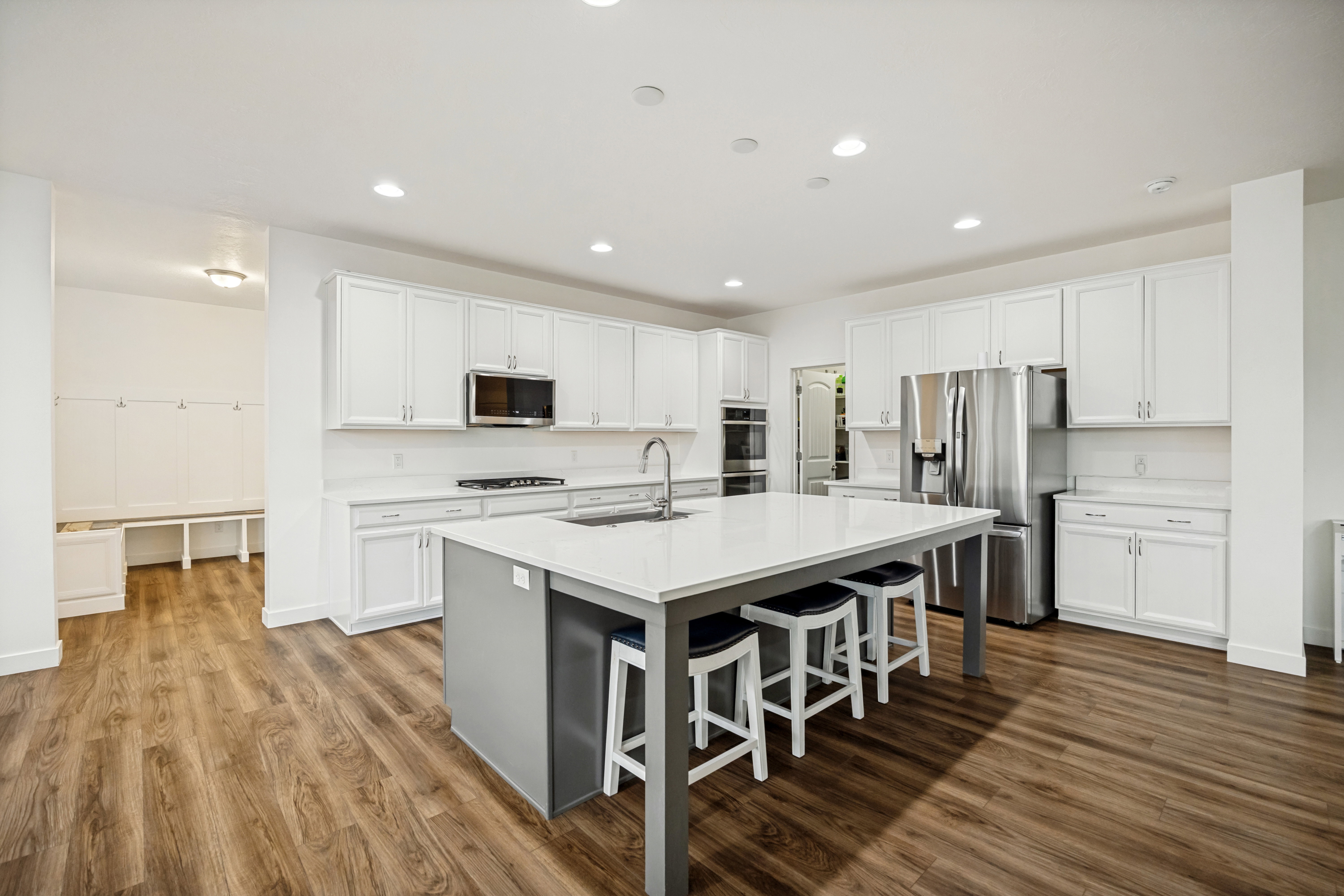Spacious kitchen featuring an expansive central island with seating, extensive white cabinetry, and wood-finish flooring