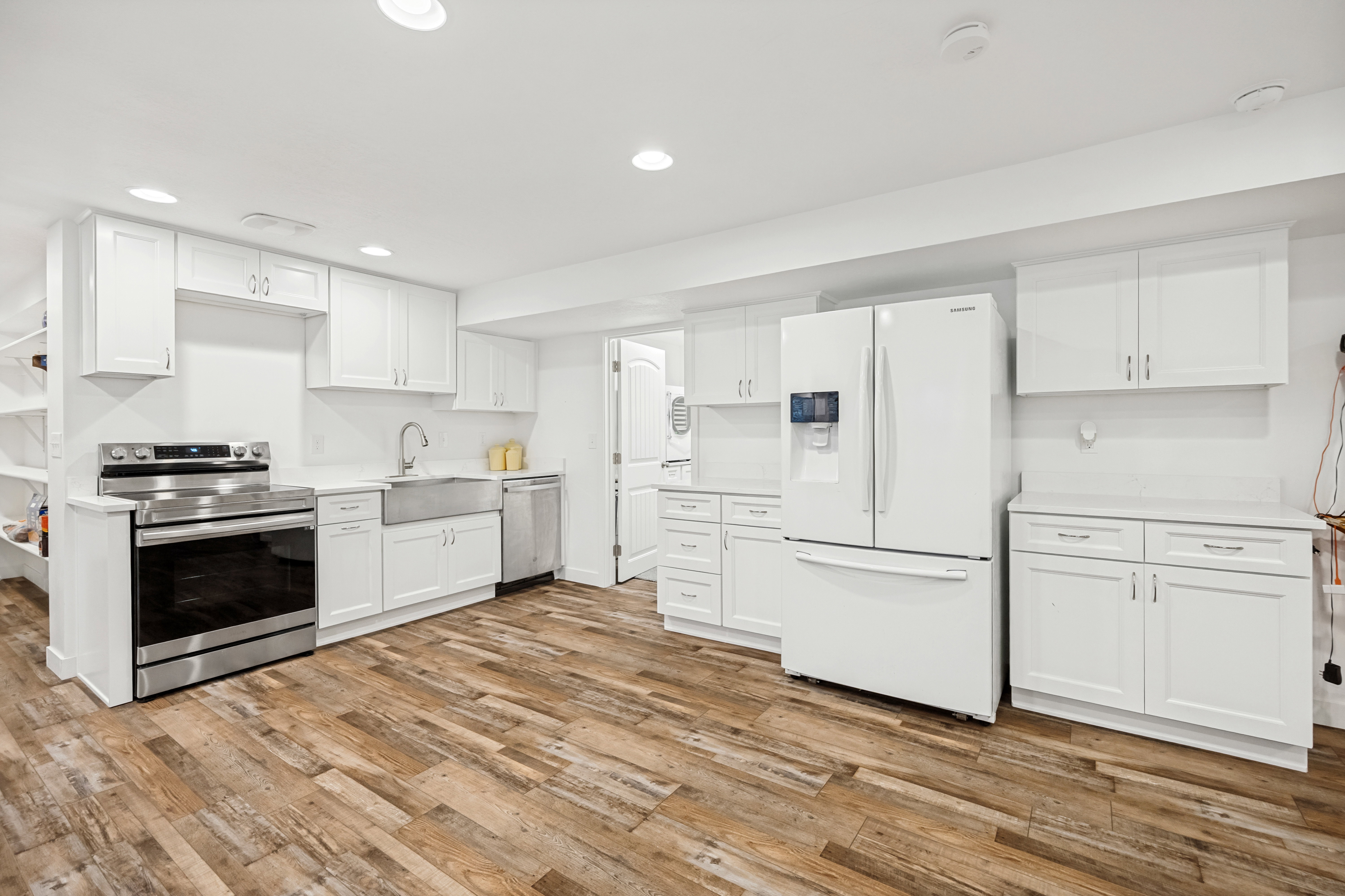 Modern kitchen featuring white shaker cabinetry, stainless steel range, farmhouse sink, white subway tile backsplash, and wood-finish flooring