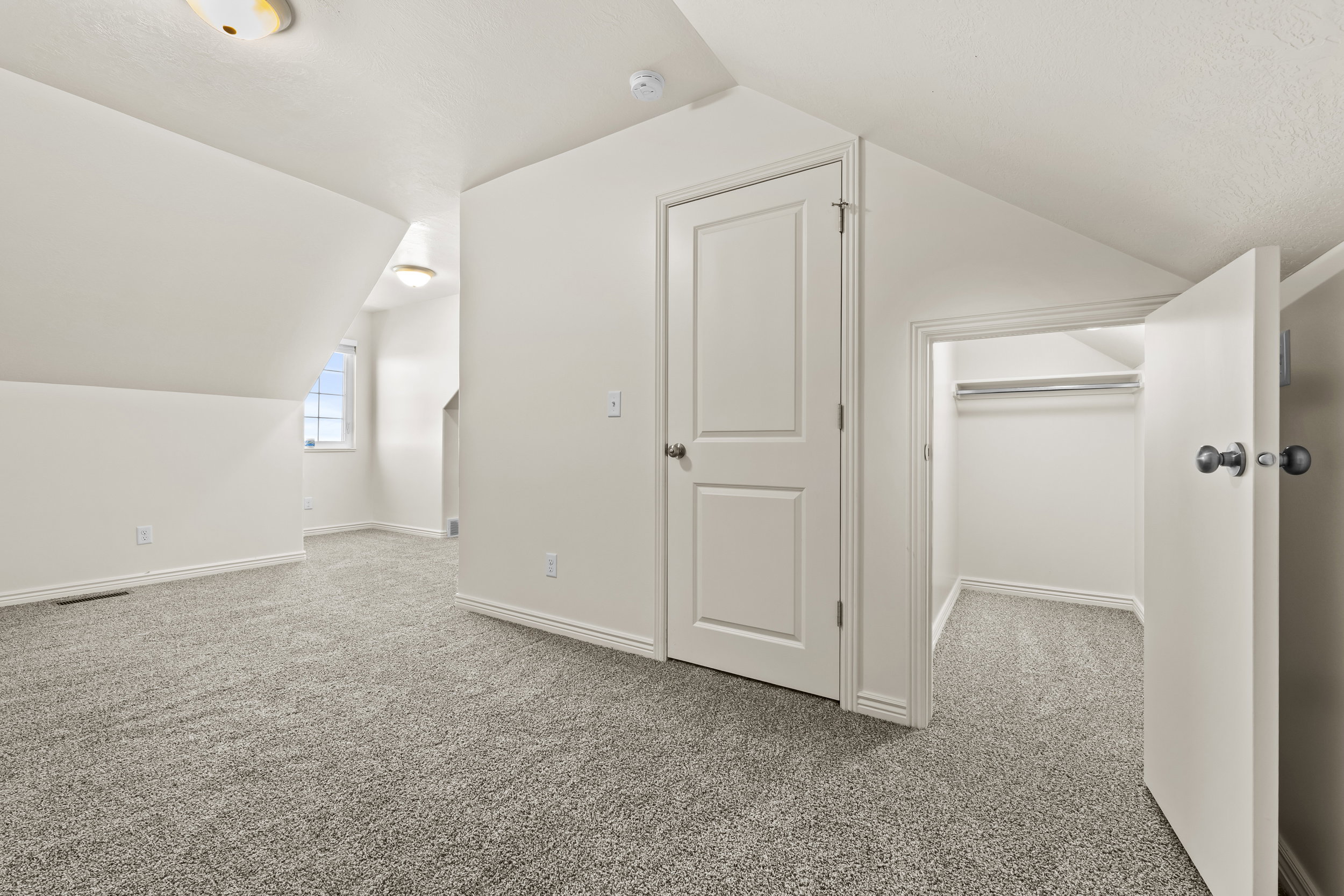 Carpeted room with a partial sloped ceiling and white painted walls