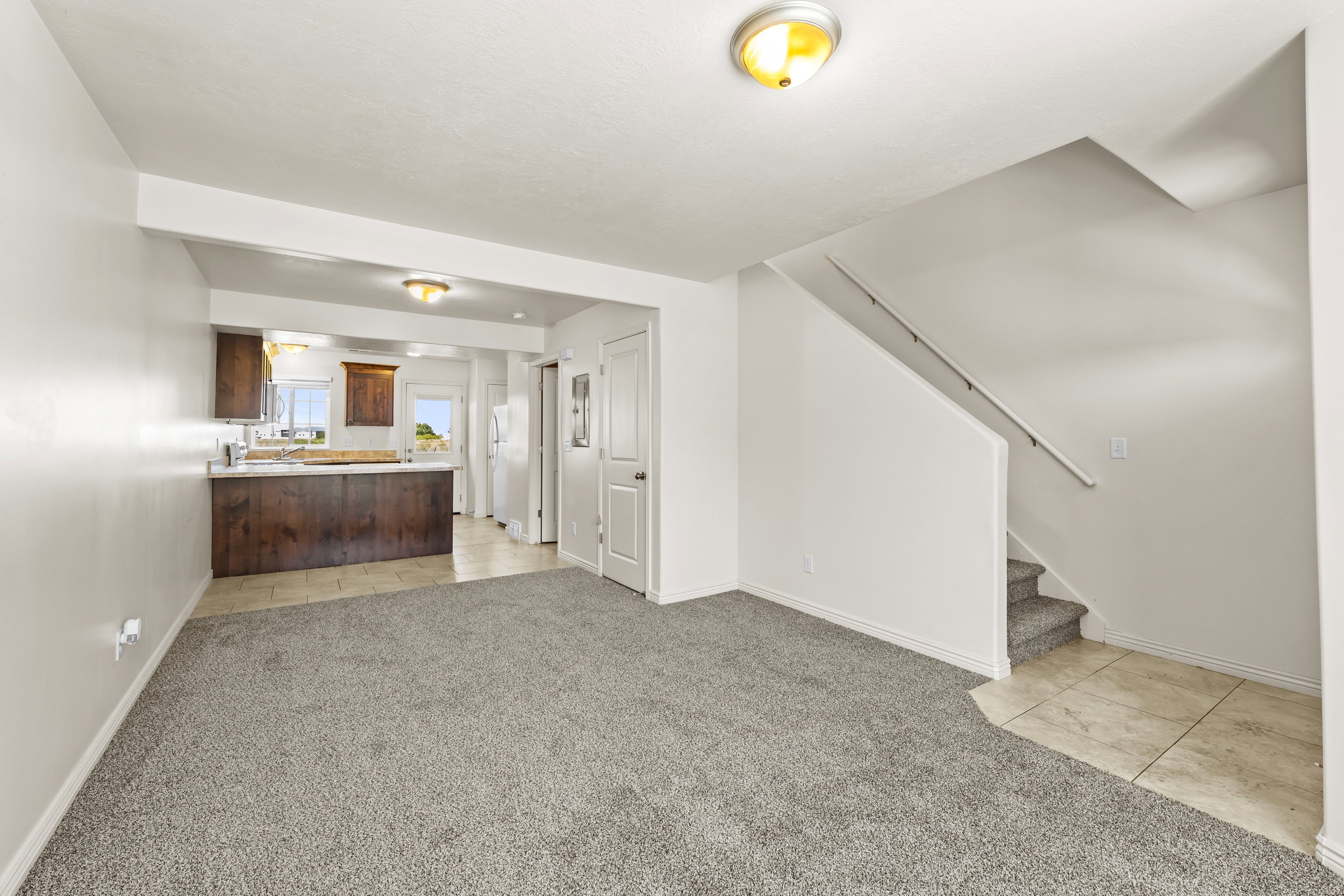 Open-concept living area featuring light gray carpeting, neutral wall paint, and a staircase with a white handrail