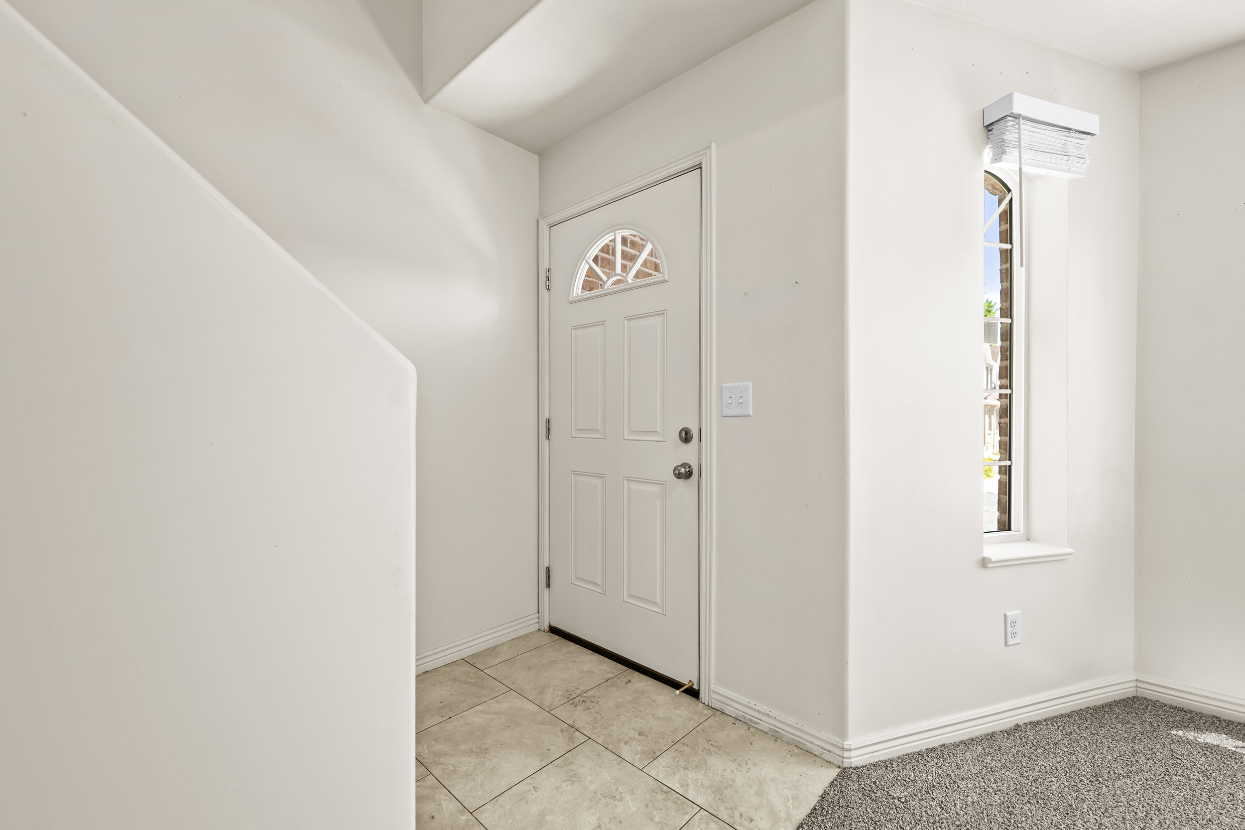 Entryway featuring a white door with an arched window insert, tiled flooring, and a tall arched window with a window sill