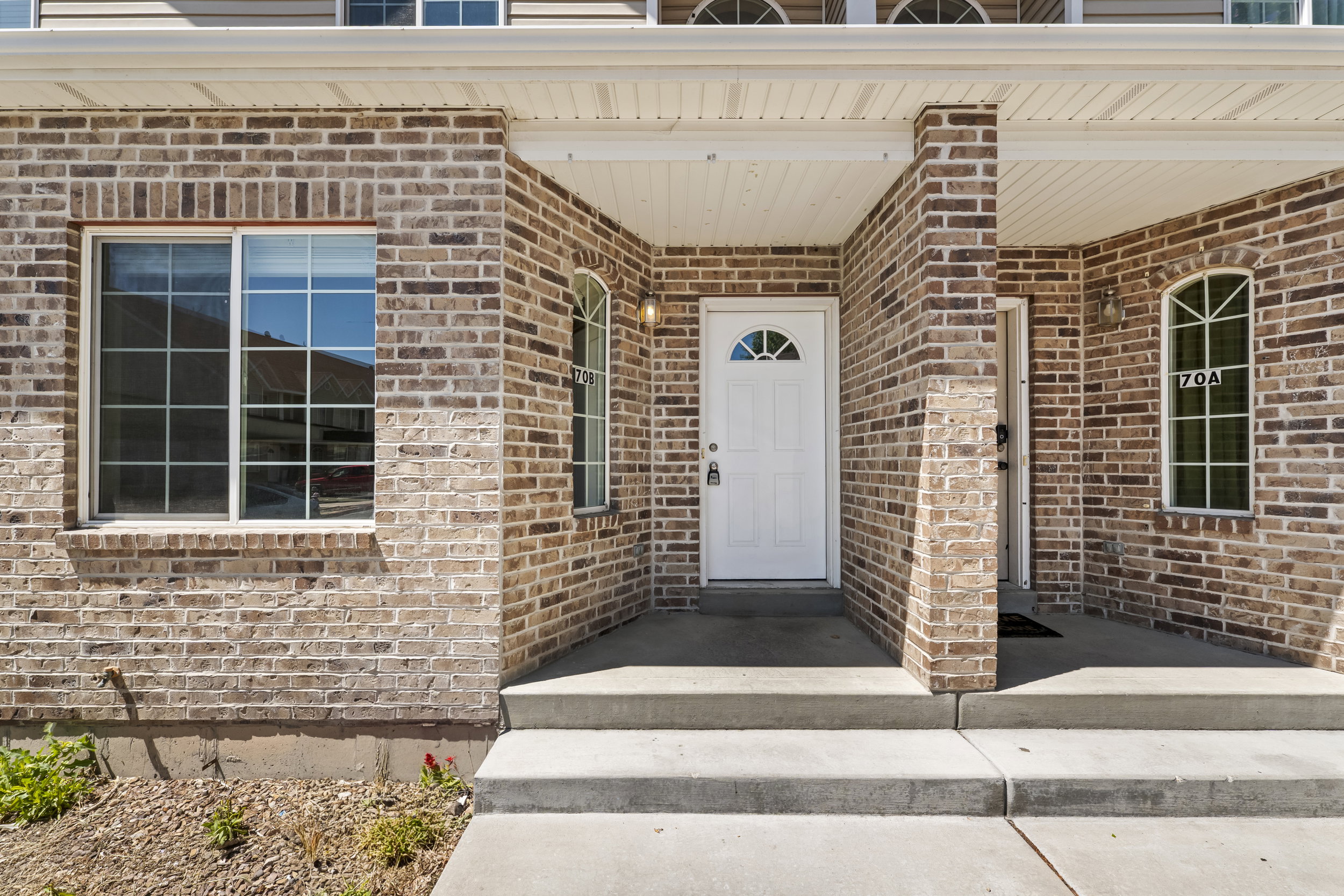 Brick exterior featuring a covered porch, white entry door with an arched window, arched side windows, a large paneled window, and concrete steps