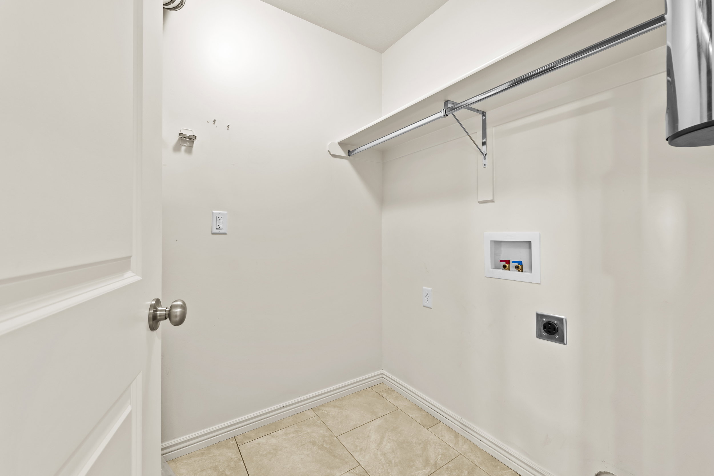 Utility area featuring ceramic tile flooring, a wall-mounted shelf, and a chrome hanging rod