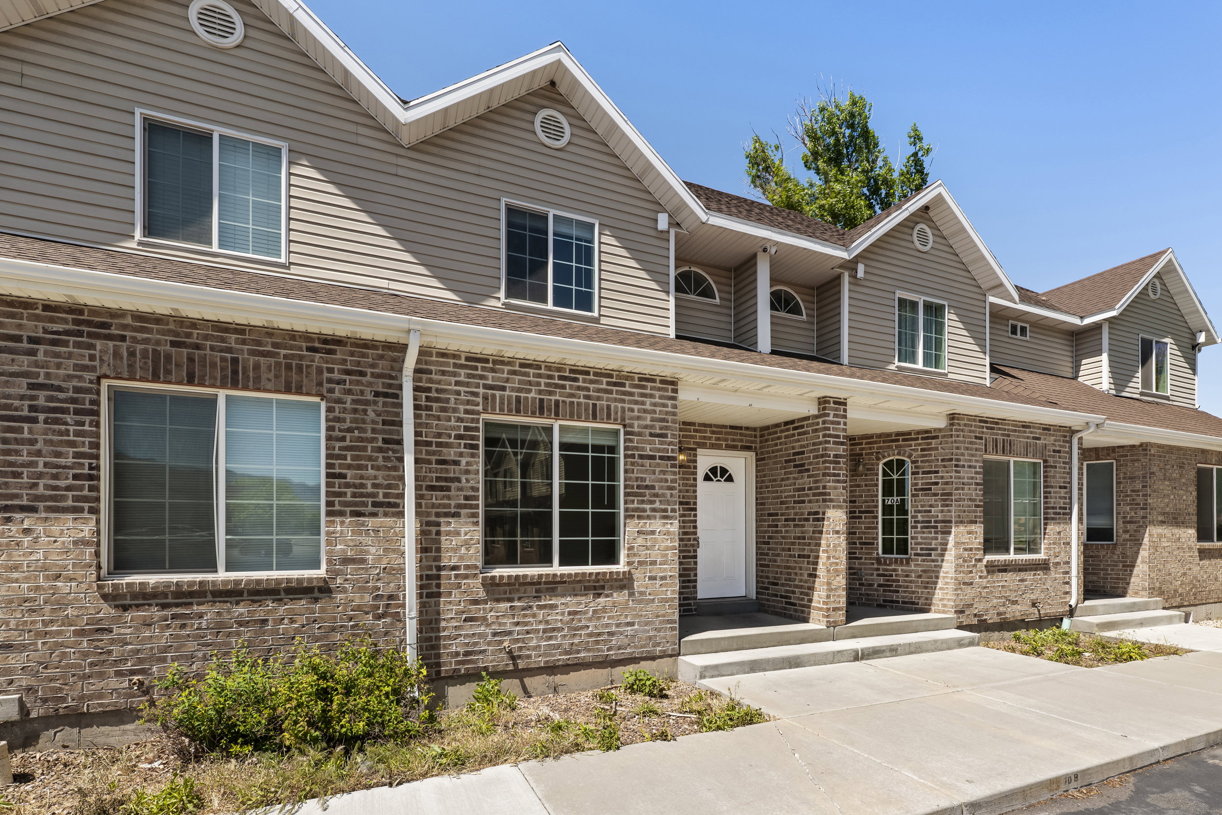 Multi-unit dwelling featuring brick and siding facade, multiple gabled rooflines, covered entryways, and white-framed windows