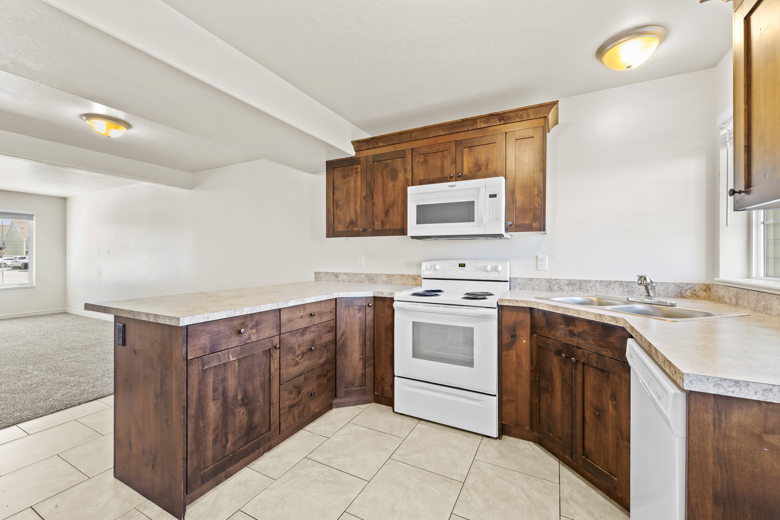 Kitchen featuring wood cabinetry, light-toned countertops, white appliances, and tiled flooring