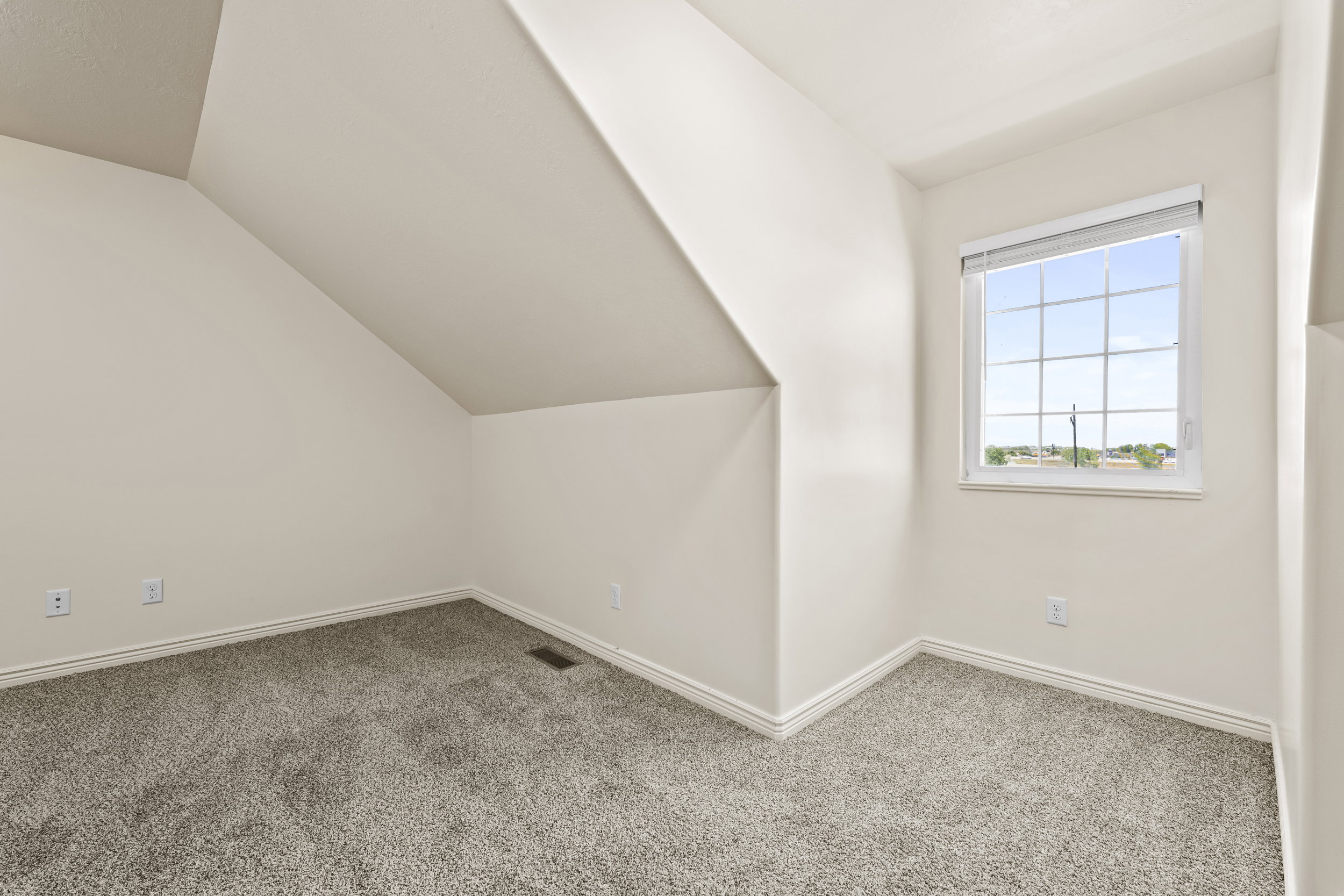 Attic room featuring a single window with gridded panes, light gray carpeting, neutral wall paint, white baseboards, and sloped ceiling details