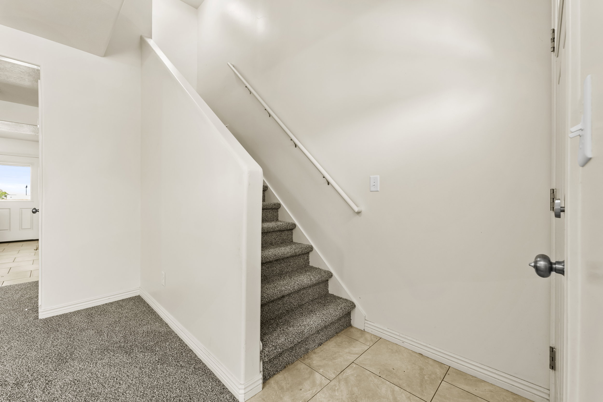 Carpeted staircase with a white handrail, complemented by neutral wall finishes and white baseboards