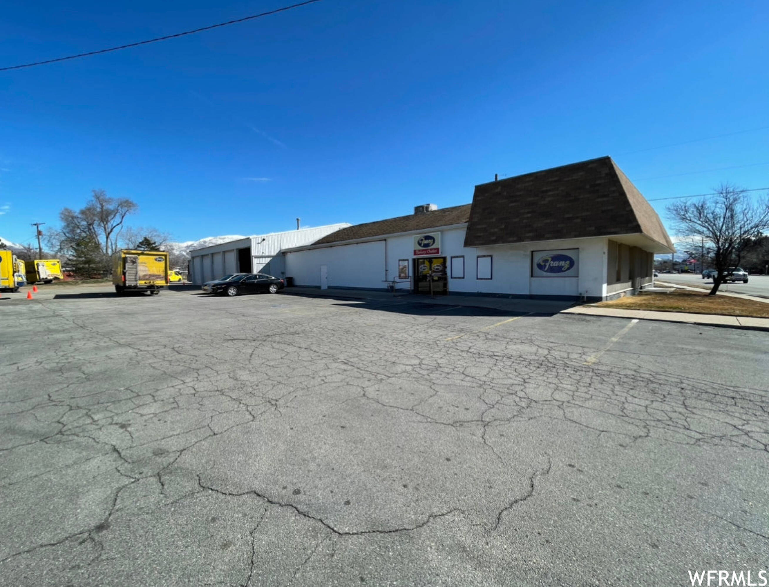 Commercial building featuring a prominent brown shingle roof, white exterior walls, and a large paved parking area