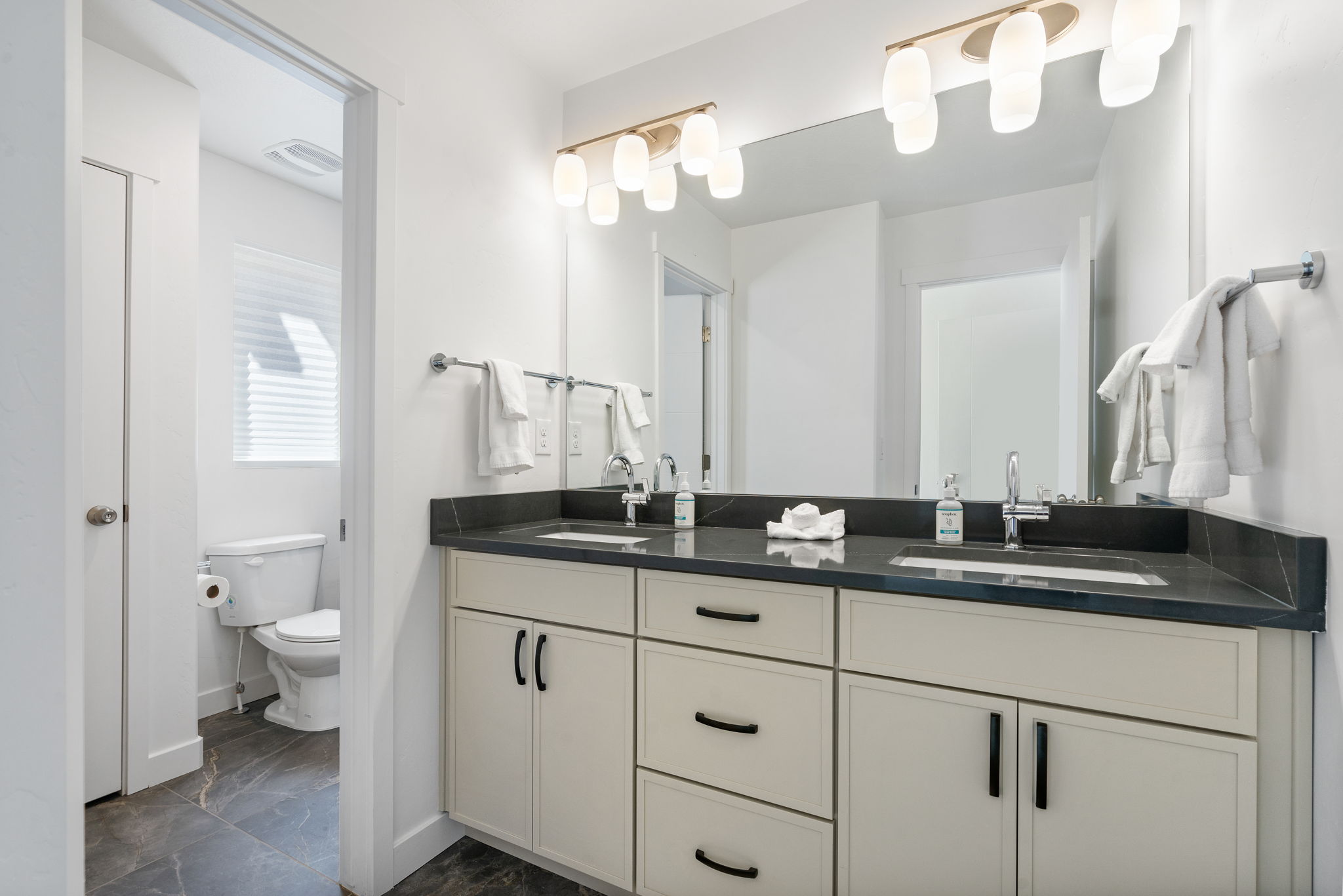 Double vanity with an integrated rectangular sink, dark countertop, and warm-toned light fixtures