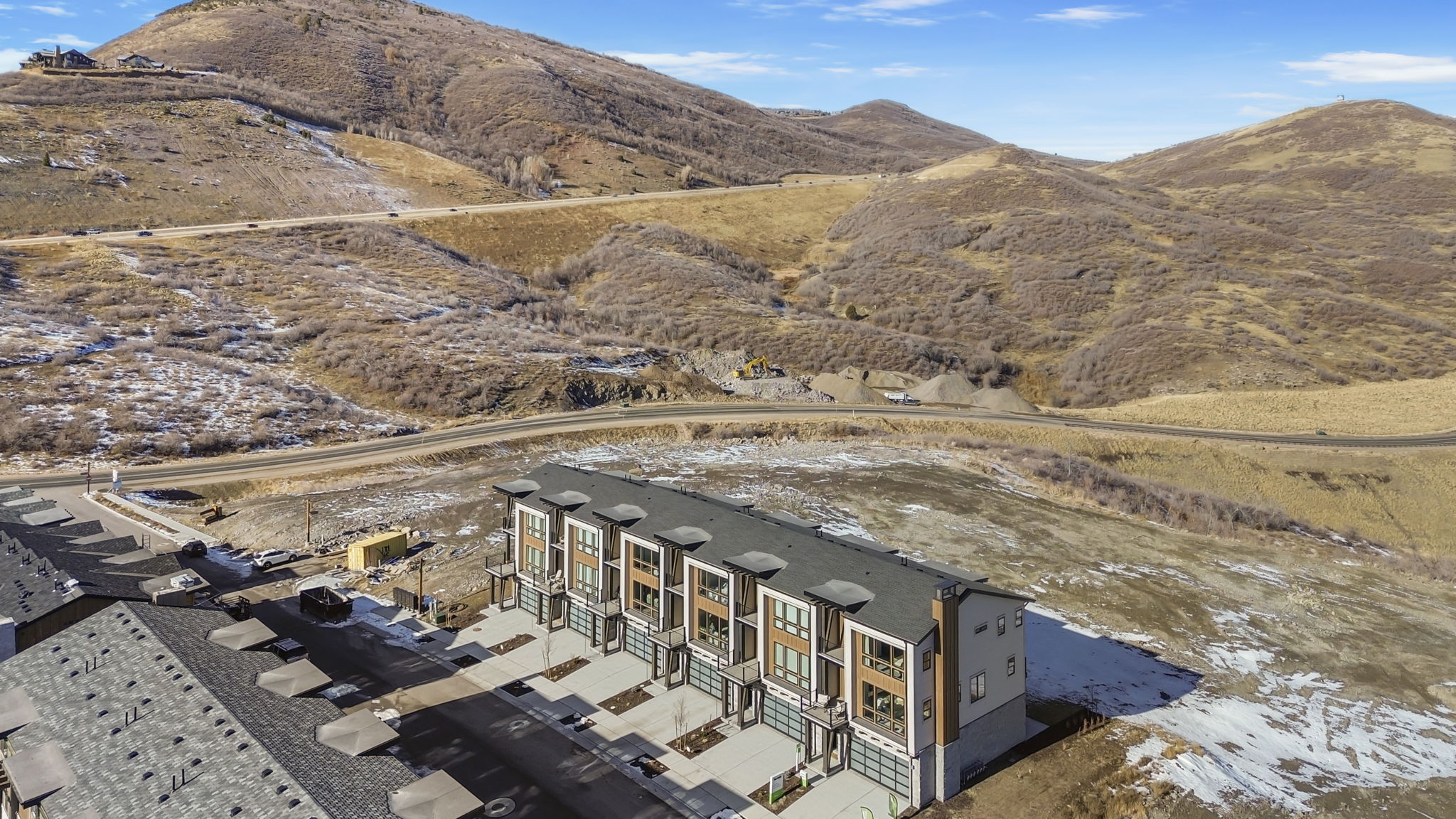 Contemporary townhome community with mountain scenery, featuring multi-level units, individual garages, and modern exterior finishes including wood-look siding and large windows