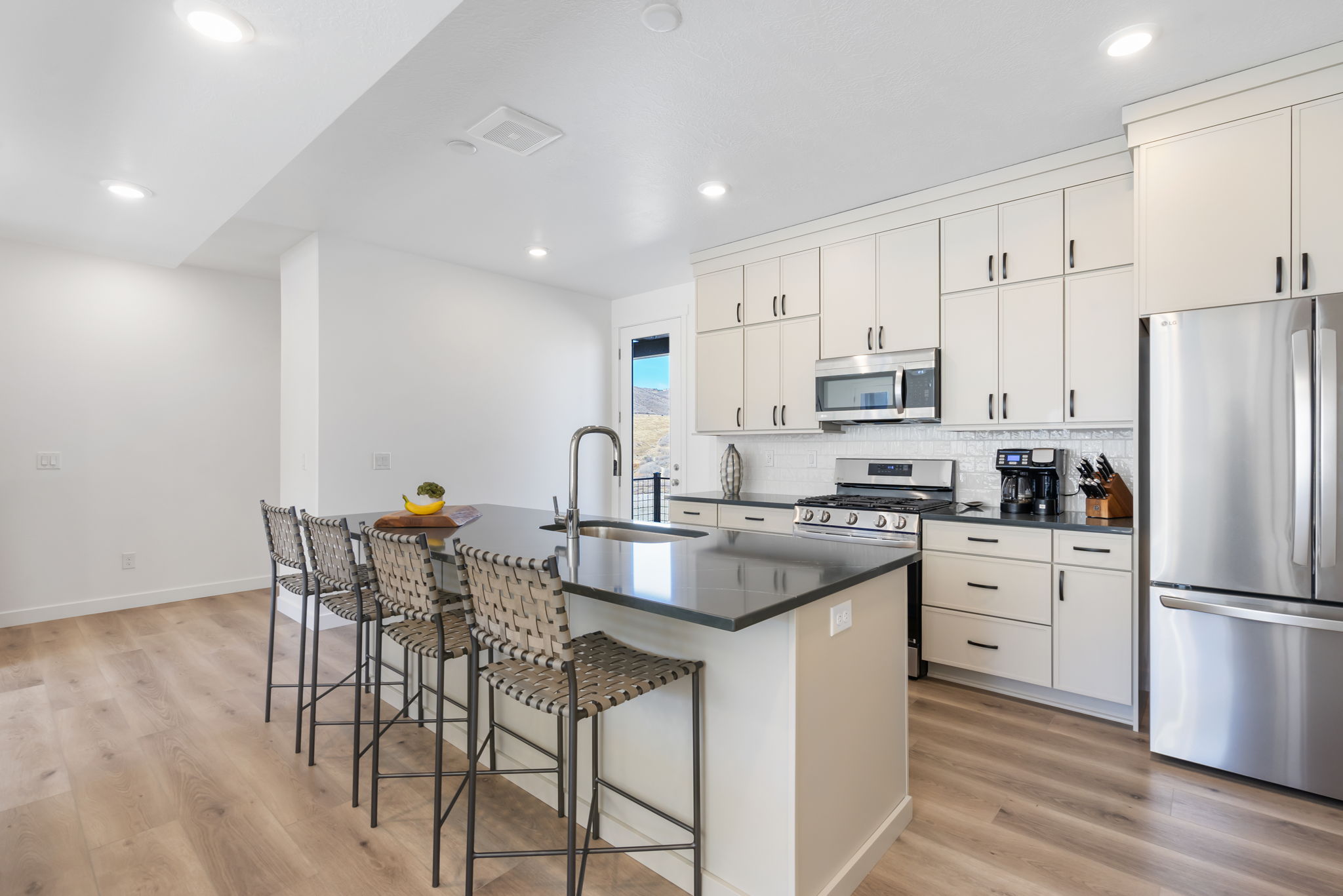 Contemporary kitchen featuring an expansive center island with seating, stainless steel appliances, white cabinetry, a subway tile backsplash, and wood-finish flooring
