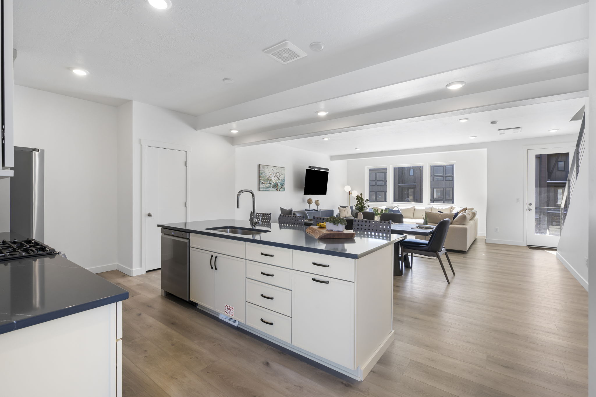 Kitchen island with dark countertop and integrated sink, stainless steel dishwasher, and white cabinetry with dark hardware